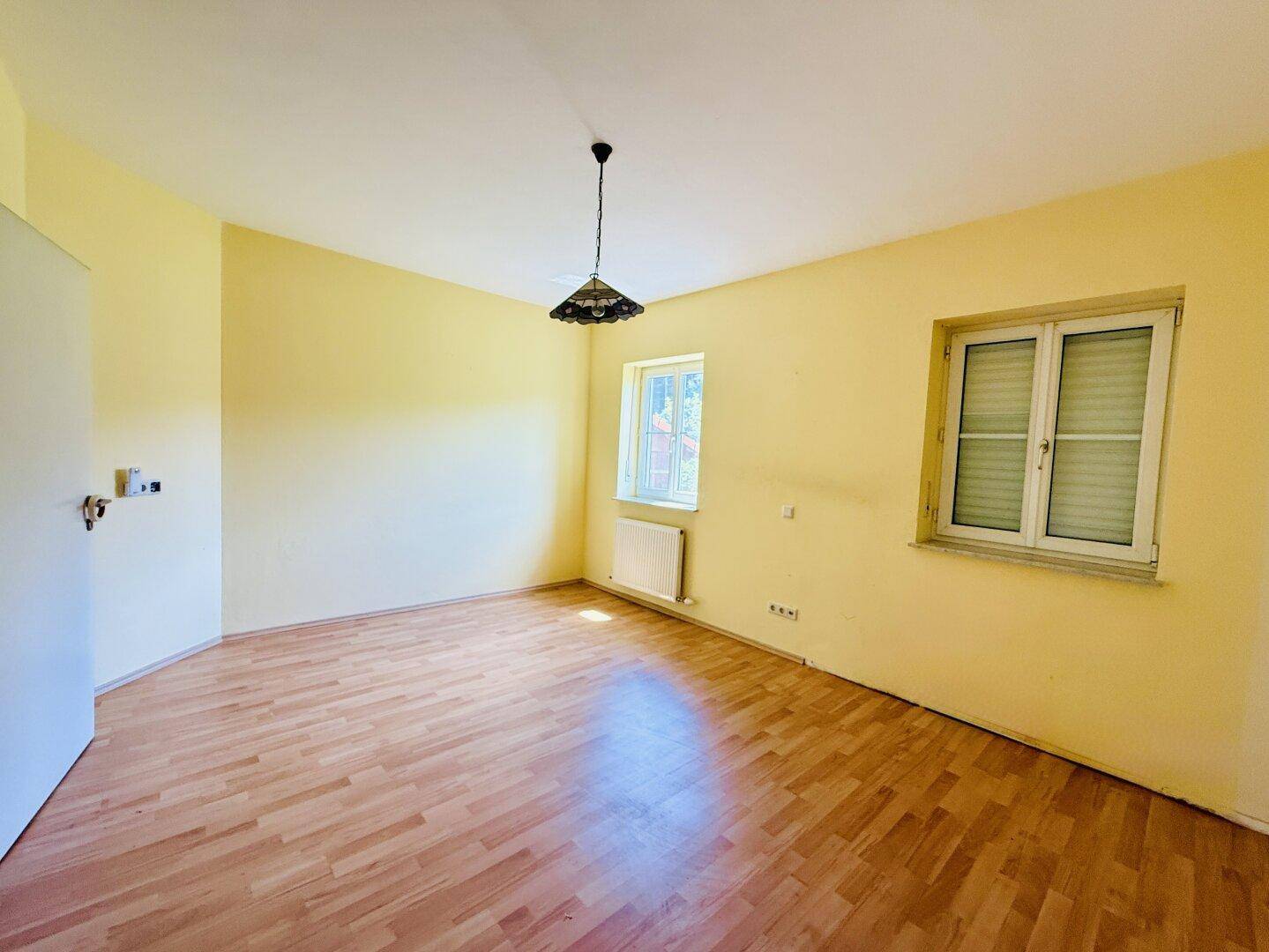 Geräumiges Schlafzimmer mit hellgelben Wänden, Holzfußboden und zwei Fenstern.