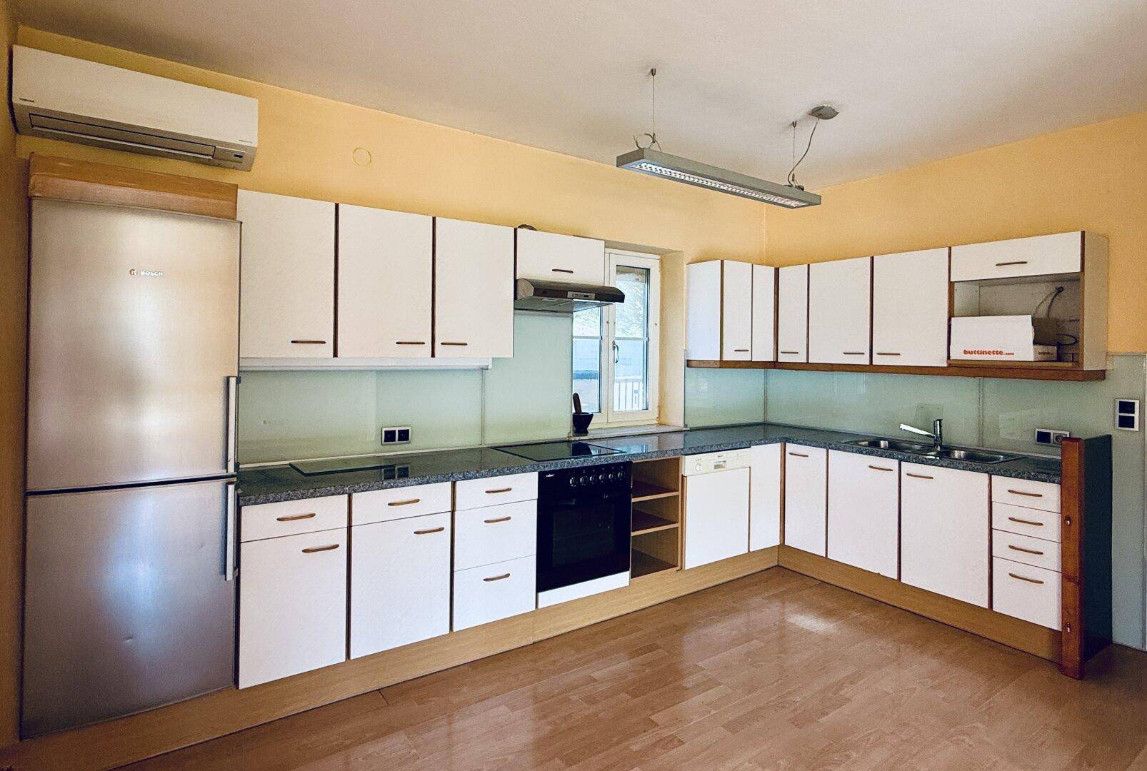 Moderne Einbauküche mit weißen Schränken, dunkler Arbeitsplatte und integrierten Geräten.