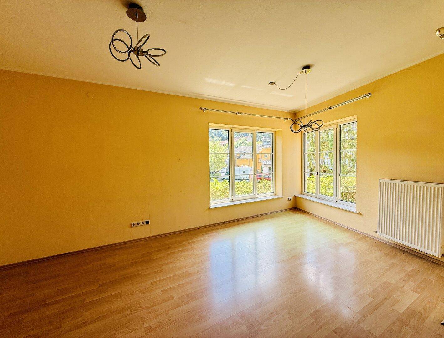 Helles Wohnzimmer mit gelben Wänden, Holzfußboden und großen Fenstern mit Ausblick.
