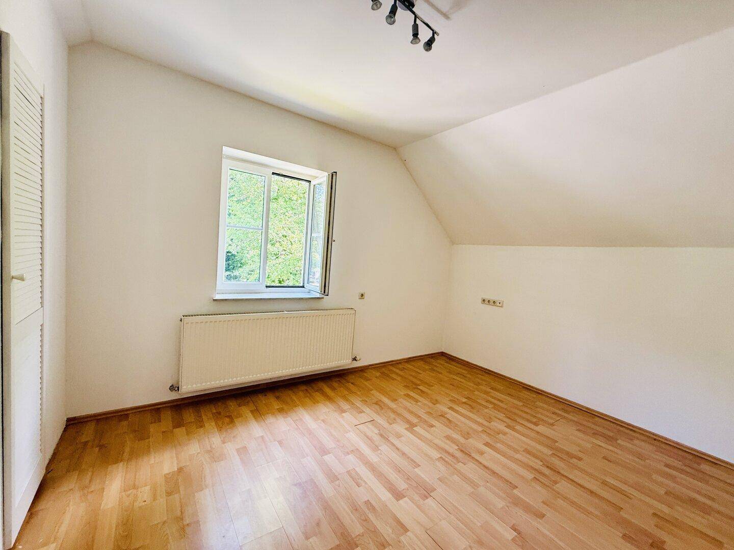 Helles Schlafzimmer im Dachgeschoss mit Holzfußboden, weiß gestrichenen Wänden und Fenster.