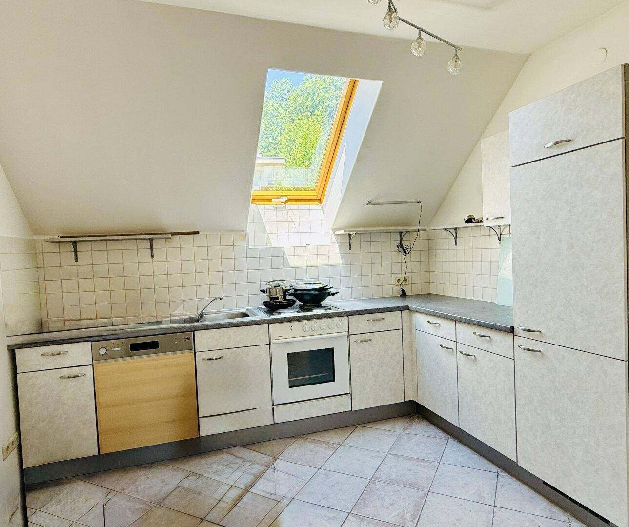 Dachgeschossküche mit Einbauschränken, Fliesenboden und einem Dachfenster für Helligkeit.