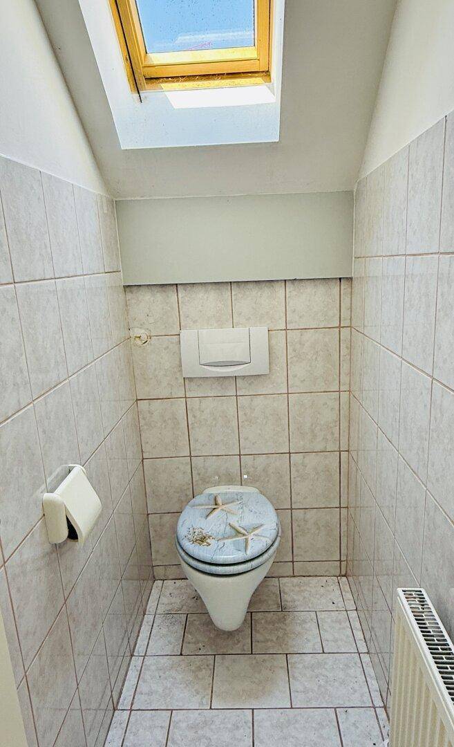 Separate Toilette mit Dachfenster, Fliesenboden und einem Heizkörper.