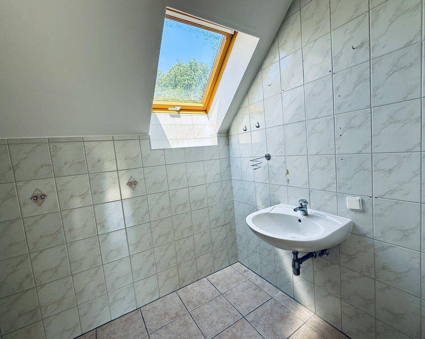 Badezimmer mit Waschbecken, Dachfenster und hellen Fliesen an den Wänden.