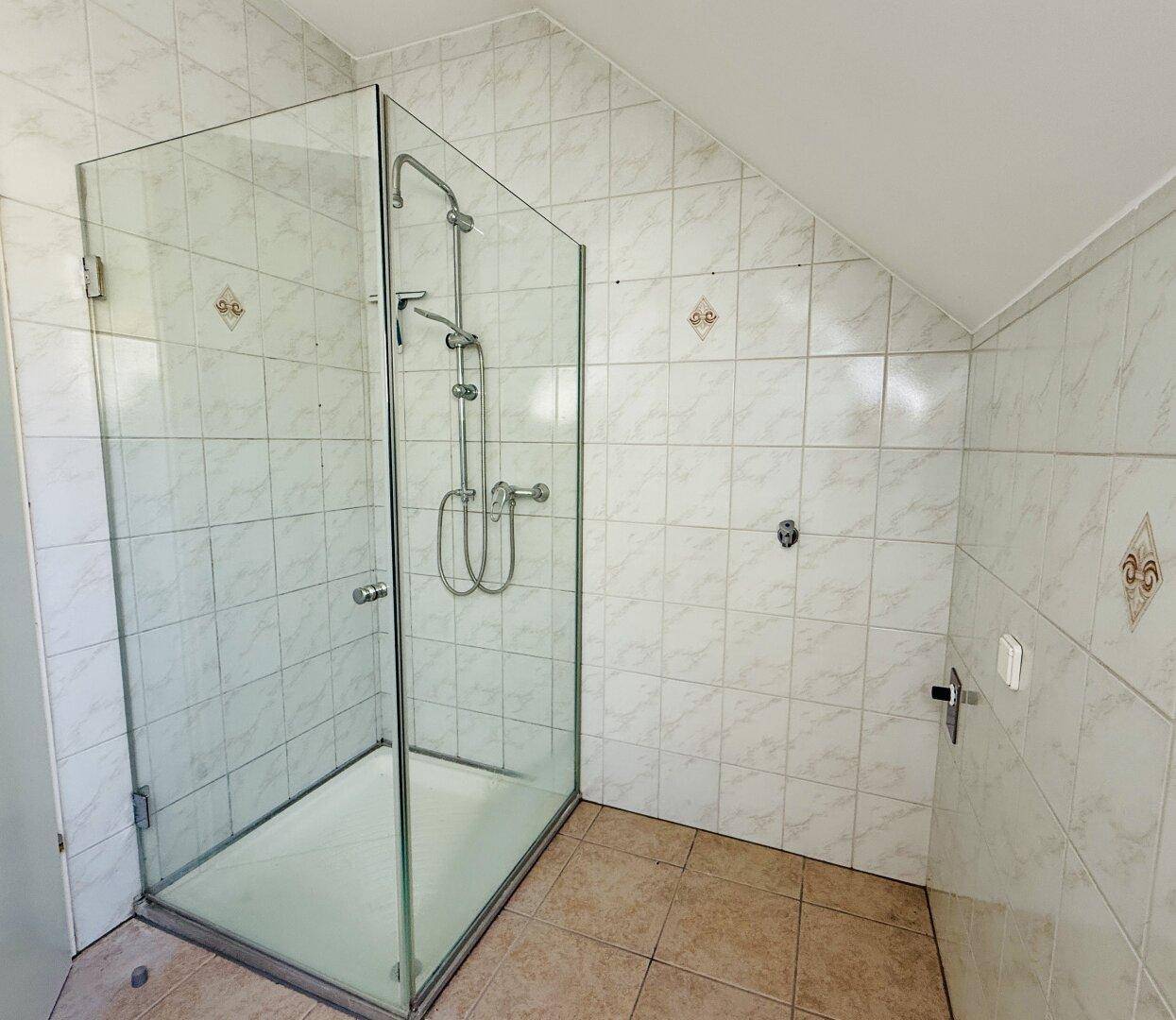 Helles Badezimmer mit Duschkabine und schrägen Wänden im Dachgeschoss.