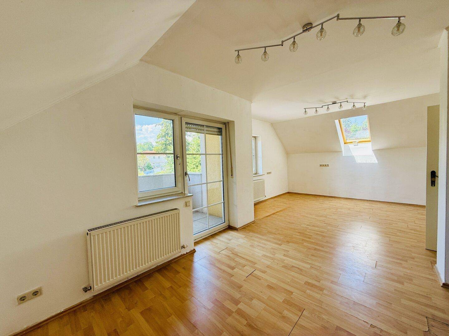 Helles Dachgeschosszimmer mit Holzfußboden, Dachfenster und Zugang zu einem Balkon.