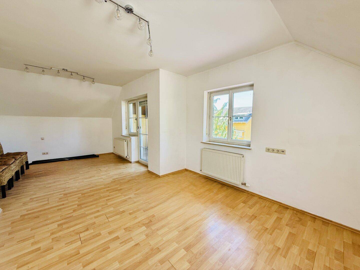 Geräumiges Dachgeschosszimmer mit Holzfußboden, weiß gestrichenen Wänden und Fenster.
