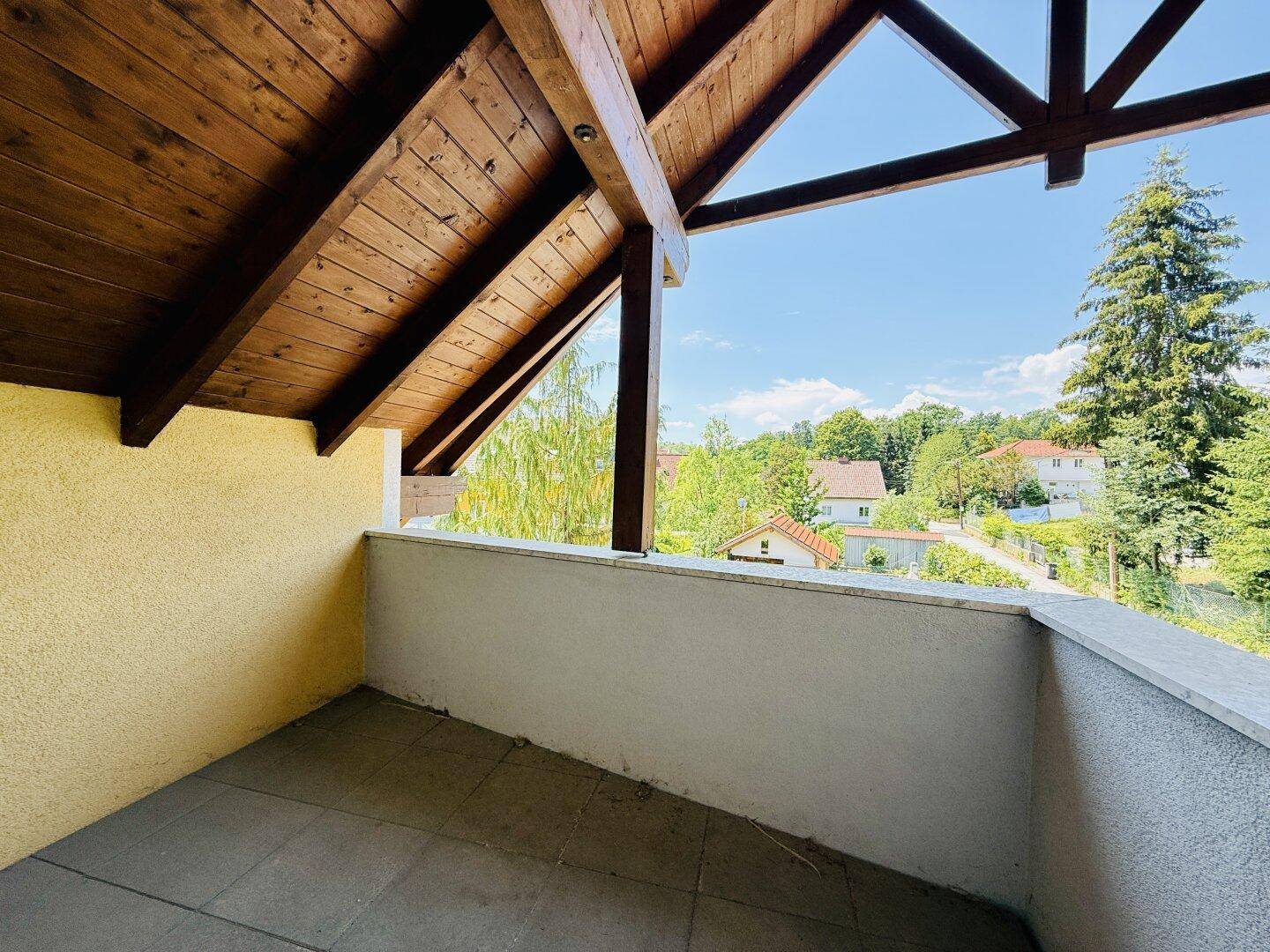 Überdachter Balkon mit Holzbalken und Blick ins Grüne.