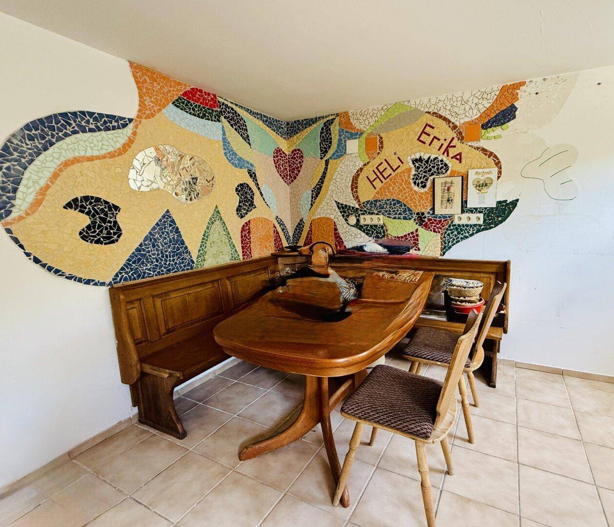 Essbereich mit rustikalen Holzmöbeln und einer farbenfrohen Mosaikwanddekoration.