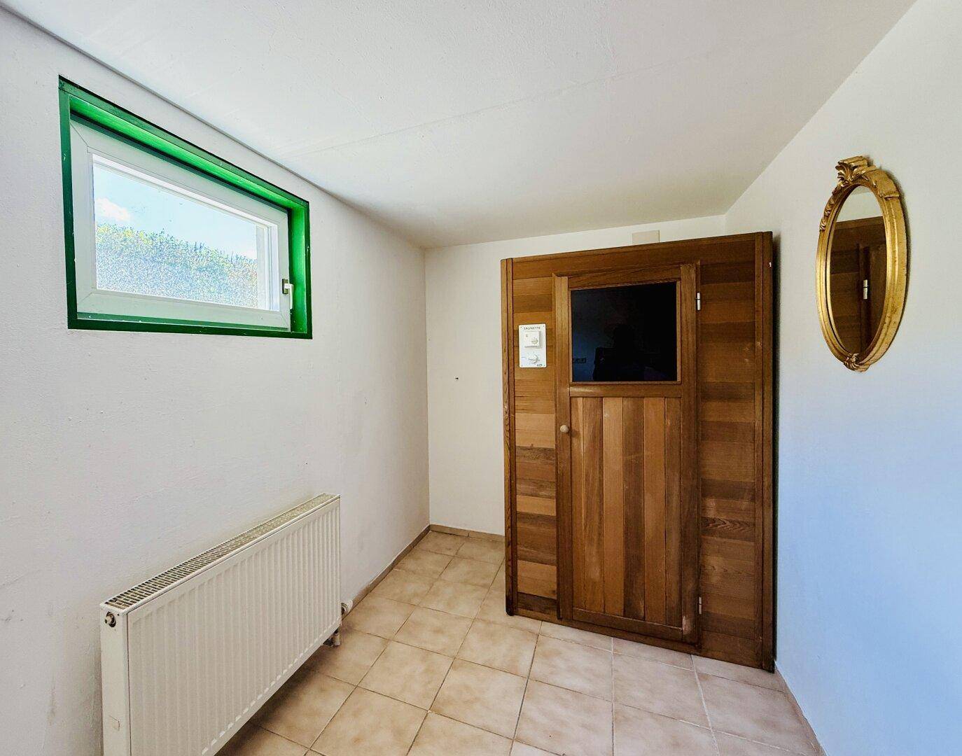 Raum mit einer Holzsauna, kleinem Fenster und Fliesenboden.