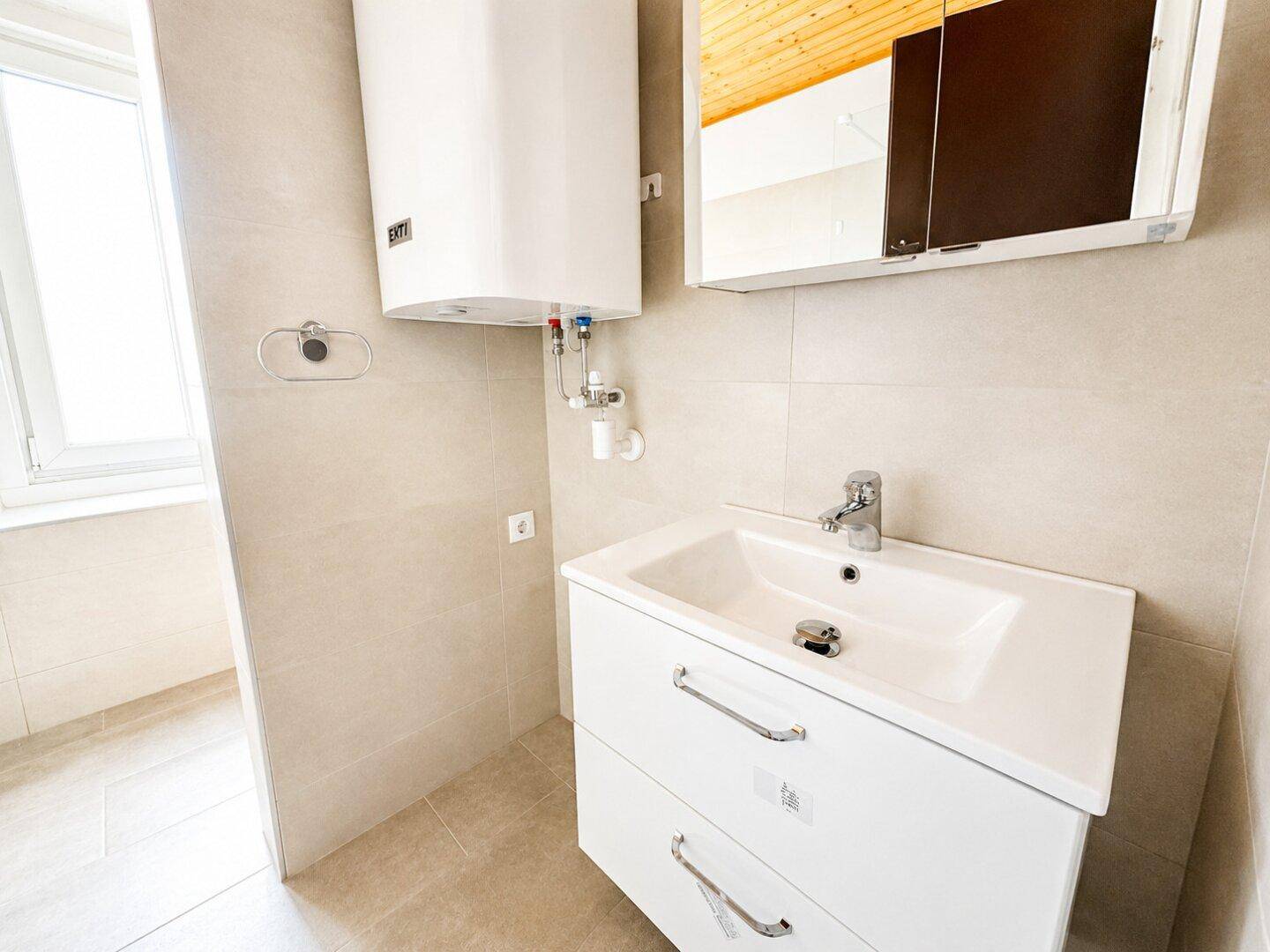 Modernes Badezimmer mit Waschbecken, Spiegelschrank und Warmwasserboiler.