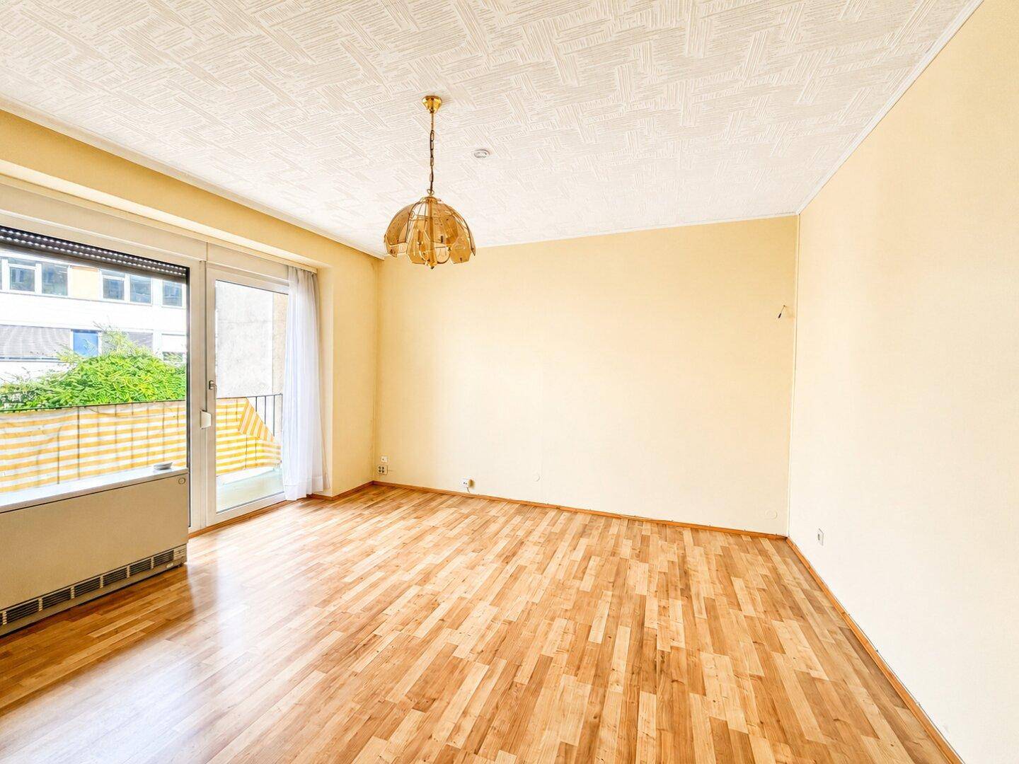 Heller Wohnraum mit Laminatboden, strukturiertem Deckenputz und Balkonzugang.