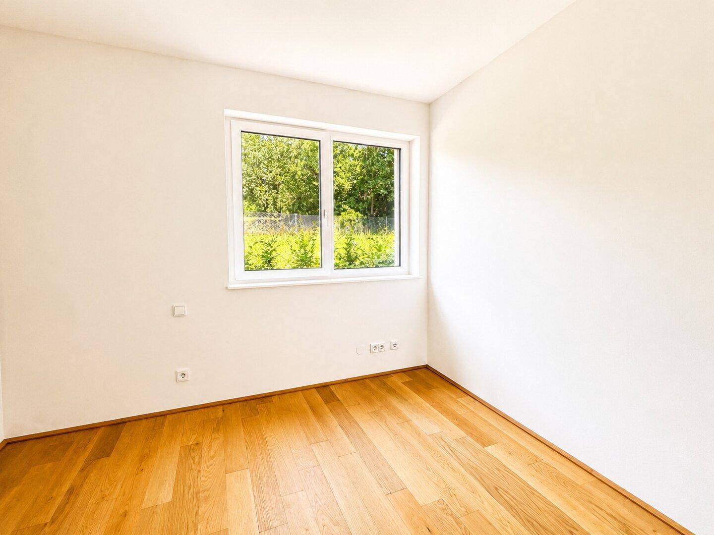 Ruhiges Schlafzimmer mit Eichenparkettboden und einem Fenster mit Blick ins Grüne.