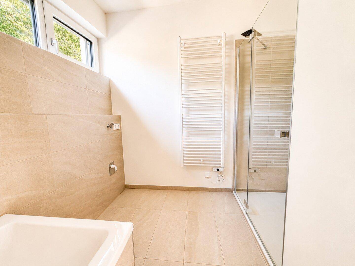Modernes Badezimmer mit Badewanne, Duschkabine, Handtuchheizkörper und Fenster.