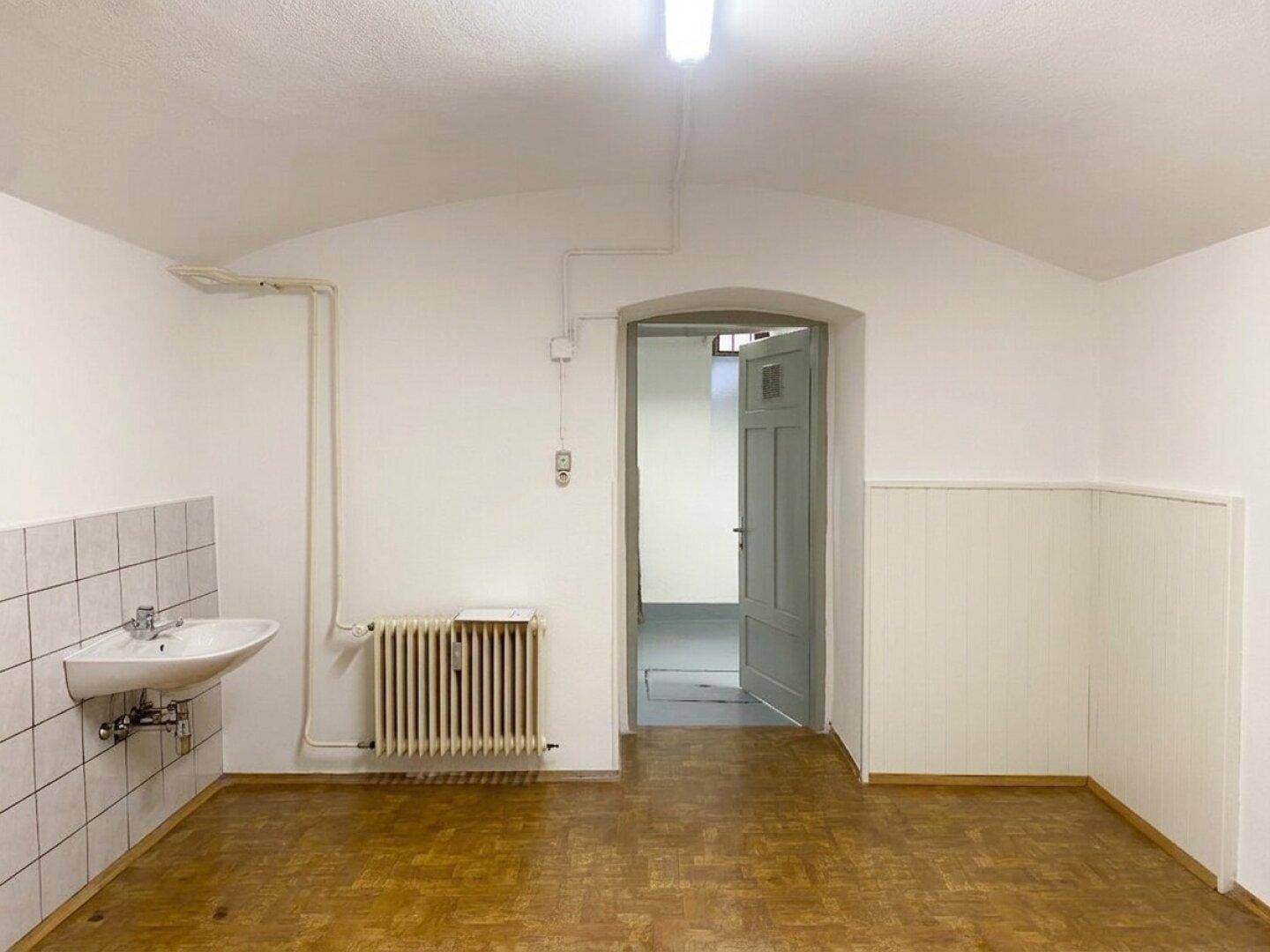 Funktionaler Kellerraum mit Waschbecken, Heizkörper und Zugang zu weiteren Räumen im Untergeschoss.