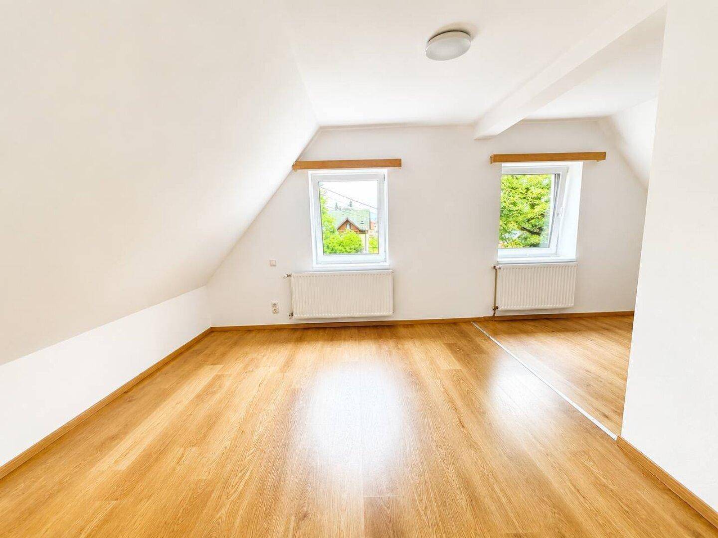 Geräumiges Zimmer im Dachgeschoss mit Holzboden und zwei Dachfenstern für viel Licht.