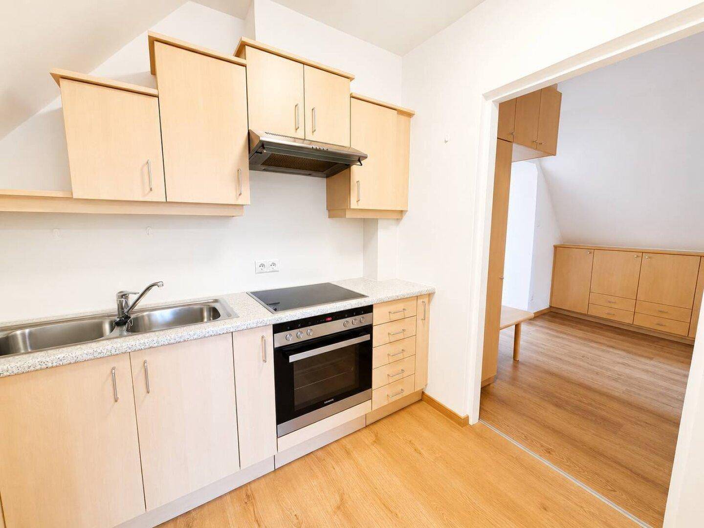 Funktionale Küche mit hellen Holzschränken, integriertem Backofen und Kochfeld.