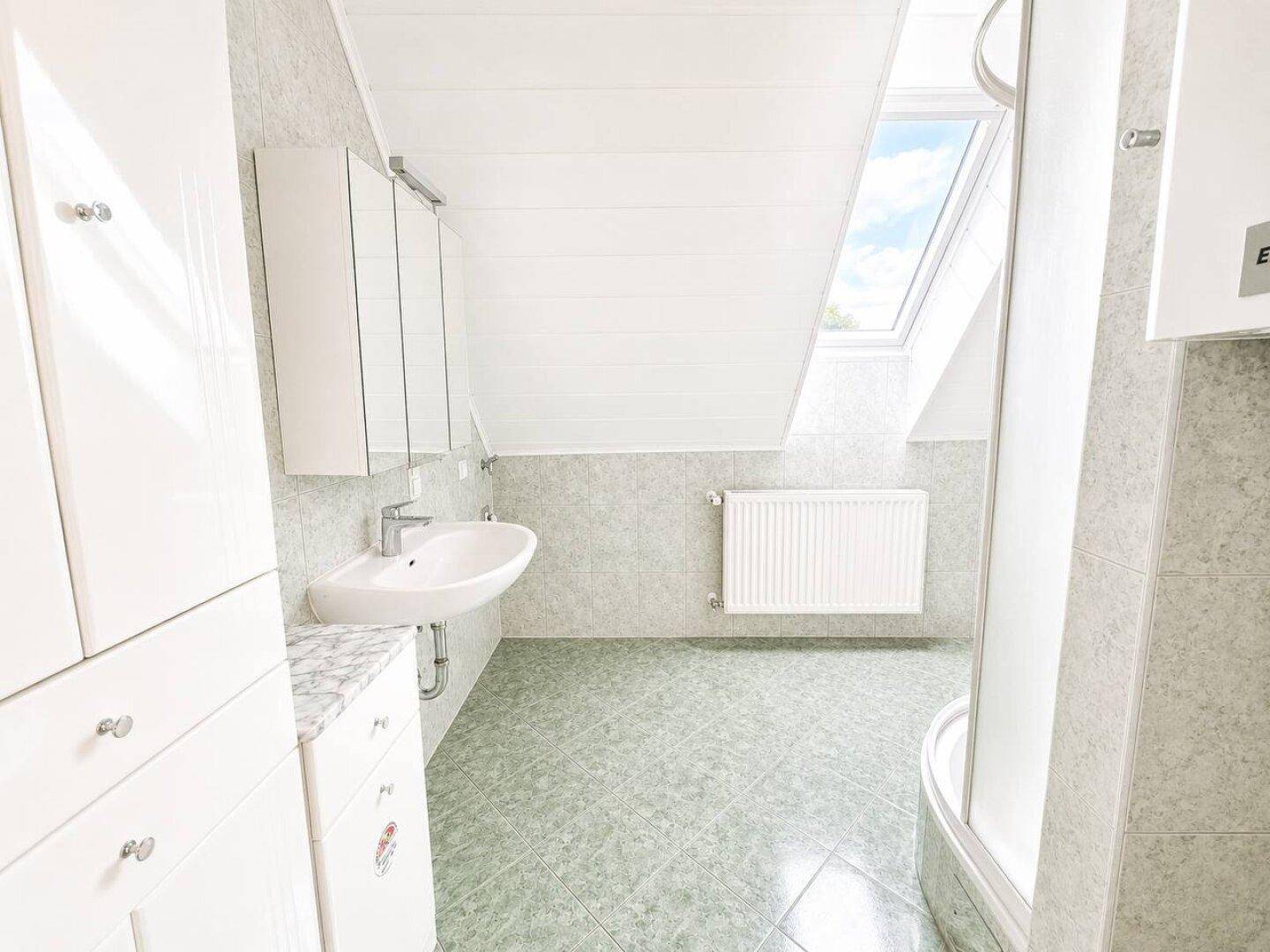 Badezimmer im Dachgeschoss mit Dusche, Waschbecken und Dachfenster für Tageslicht.