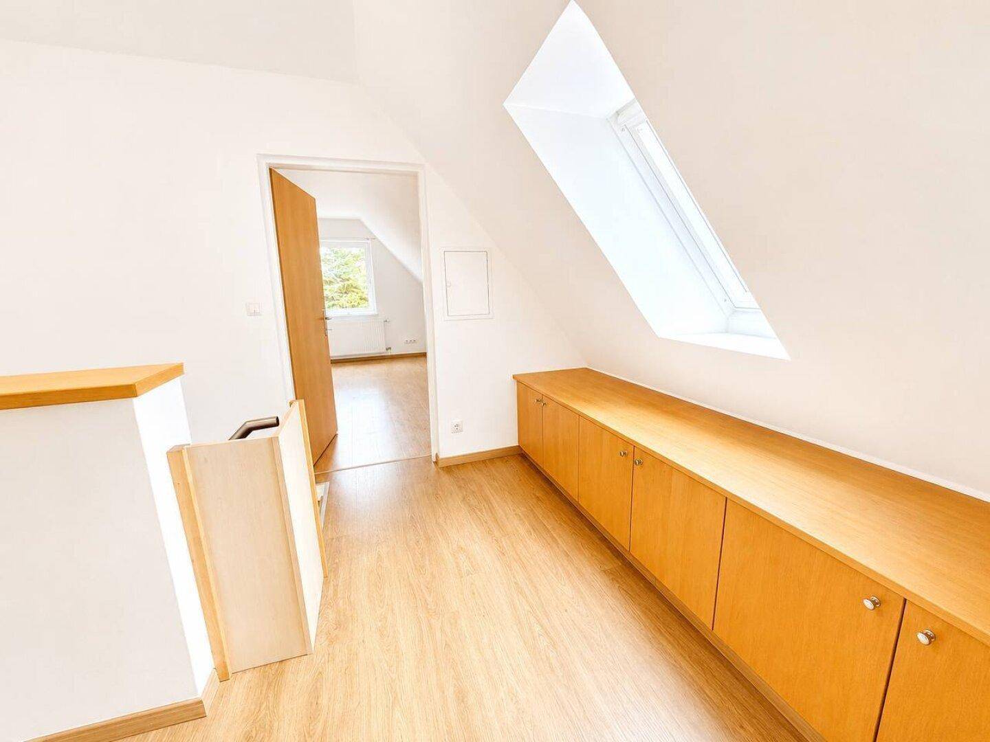 Heller Dachgeschossflur mit Einbauschränken, Holzboden und einem schrägen Dachfenster.