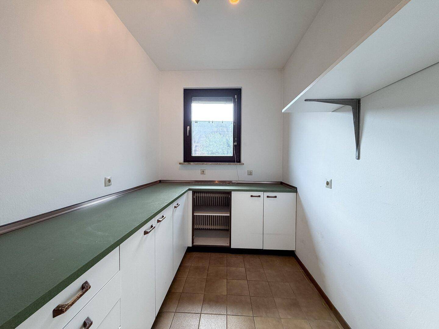 Praktischer Hauswirtschaftsraum mit einfachen Schränken, Arbeitsplatte und Fenster.