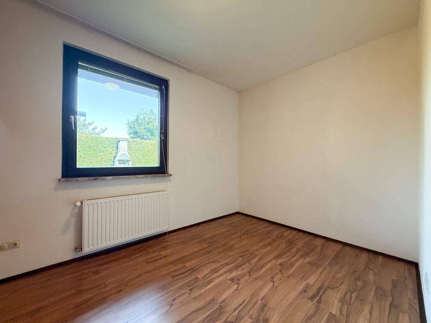 Helles Zimmer mit Laminatboden und großem Fenster mit Blick ins Grüne.