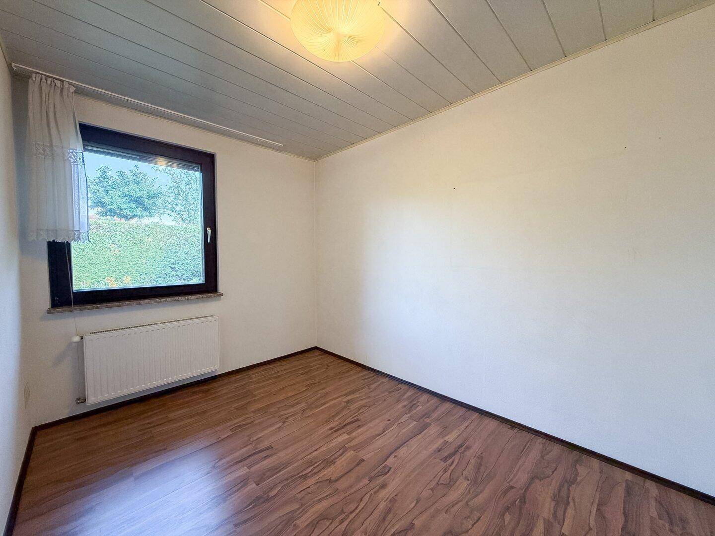Kleines Zimmer mit Laminatboden und Fenster mit Blick auf die Hecke.