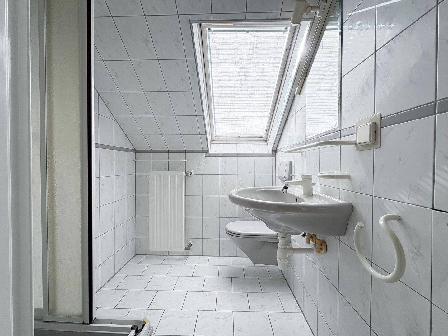 Helles Badezimmer im Dachgeschoss mit weißen Fliesen, Waschbecken und Dachfenster.