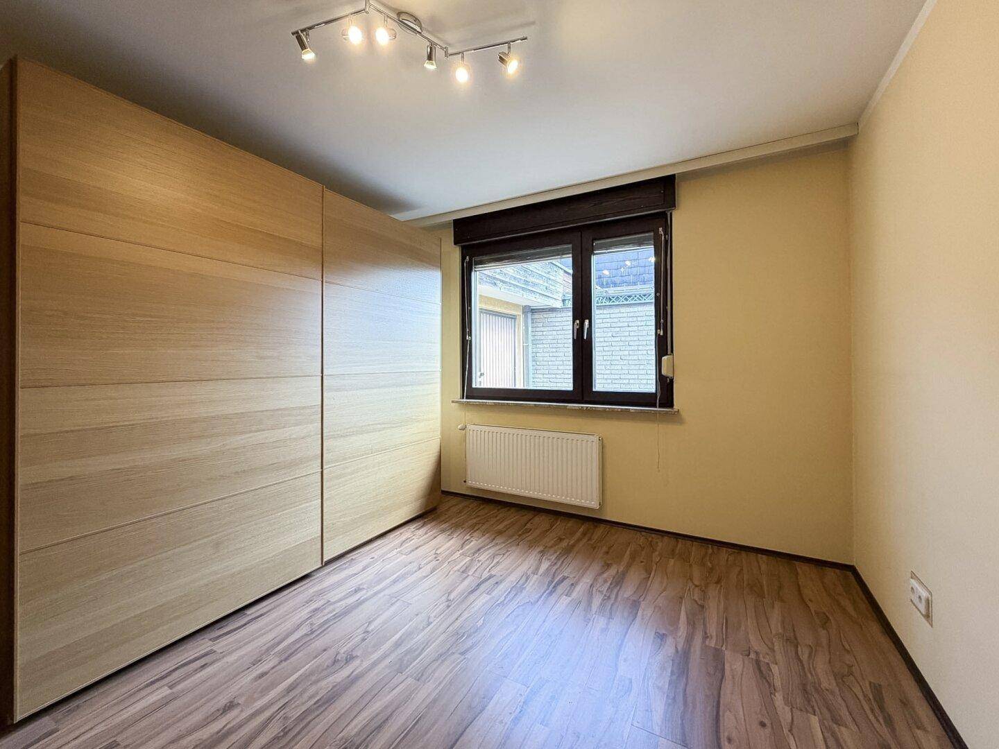 Schlafzimmer mit Laminatboden, Einbauschränken und Fenster mit Rollladen.