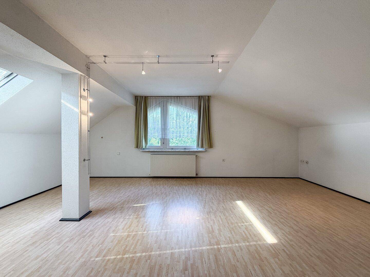 Geräumiger Dachbodenraum mit Laminatboden, Dachschrägen und großem Fenster.