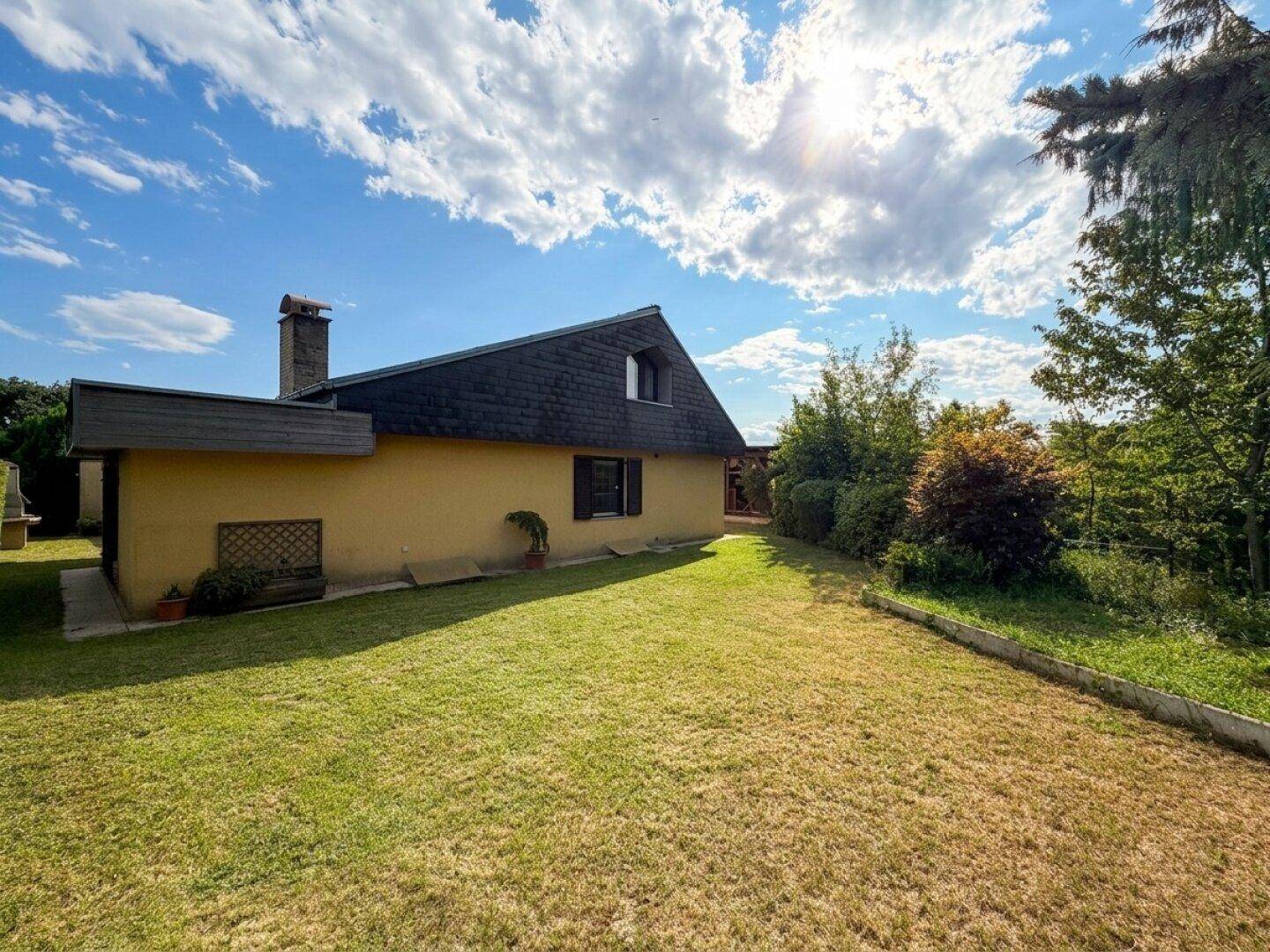 Seitenansicht des Hauses mit großem Garten und sonniger Rasenfläche.