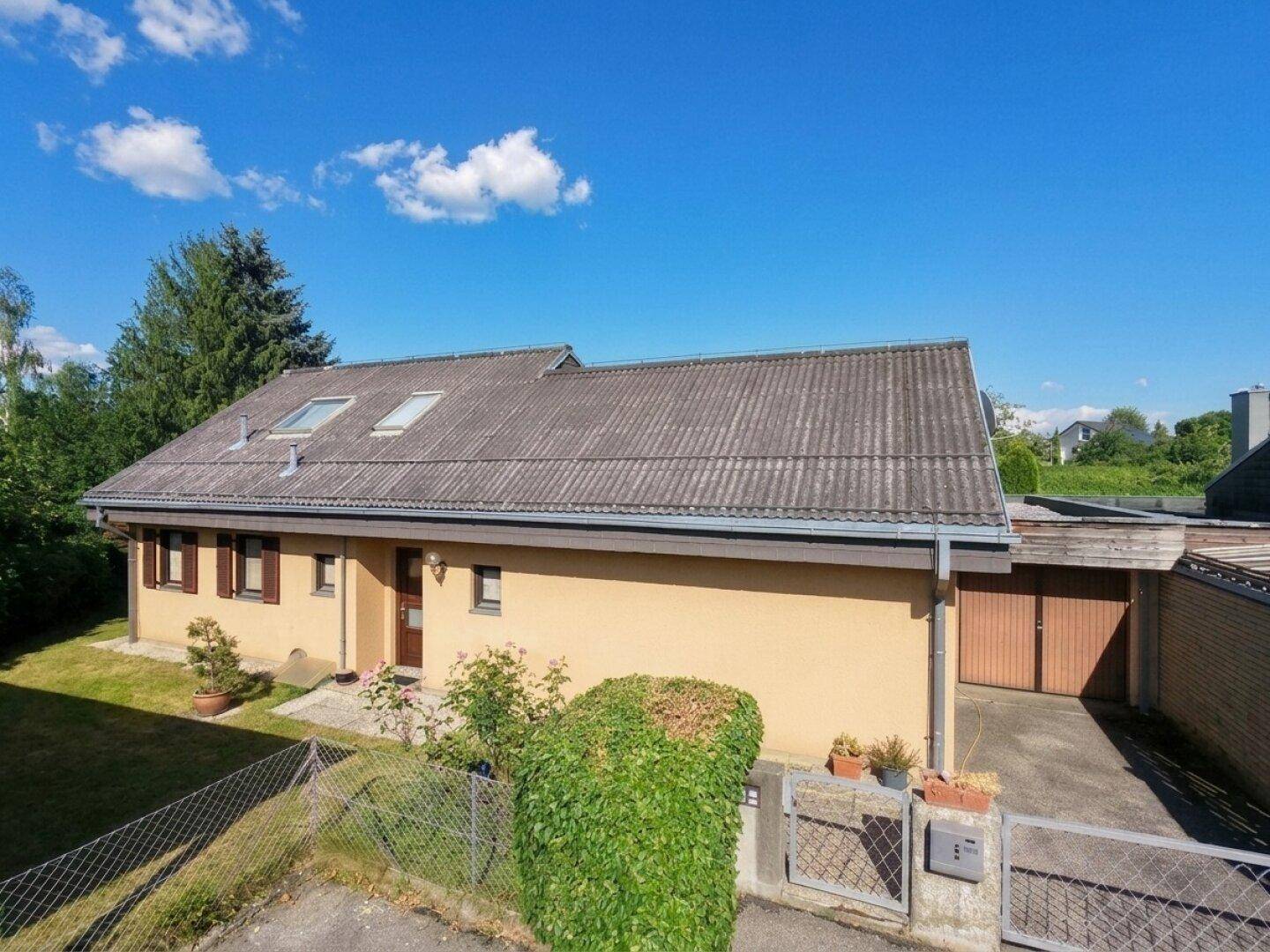 Gelbes Einfamilienhaus mit Satteldach, Vorgarten und überdachtem Stellplatz.