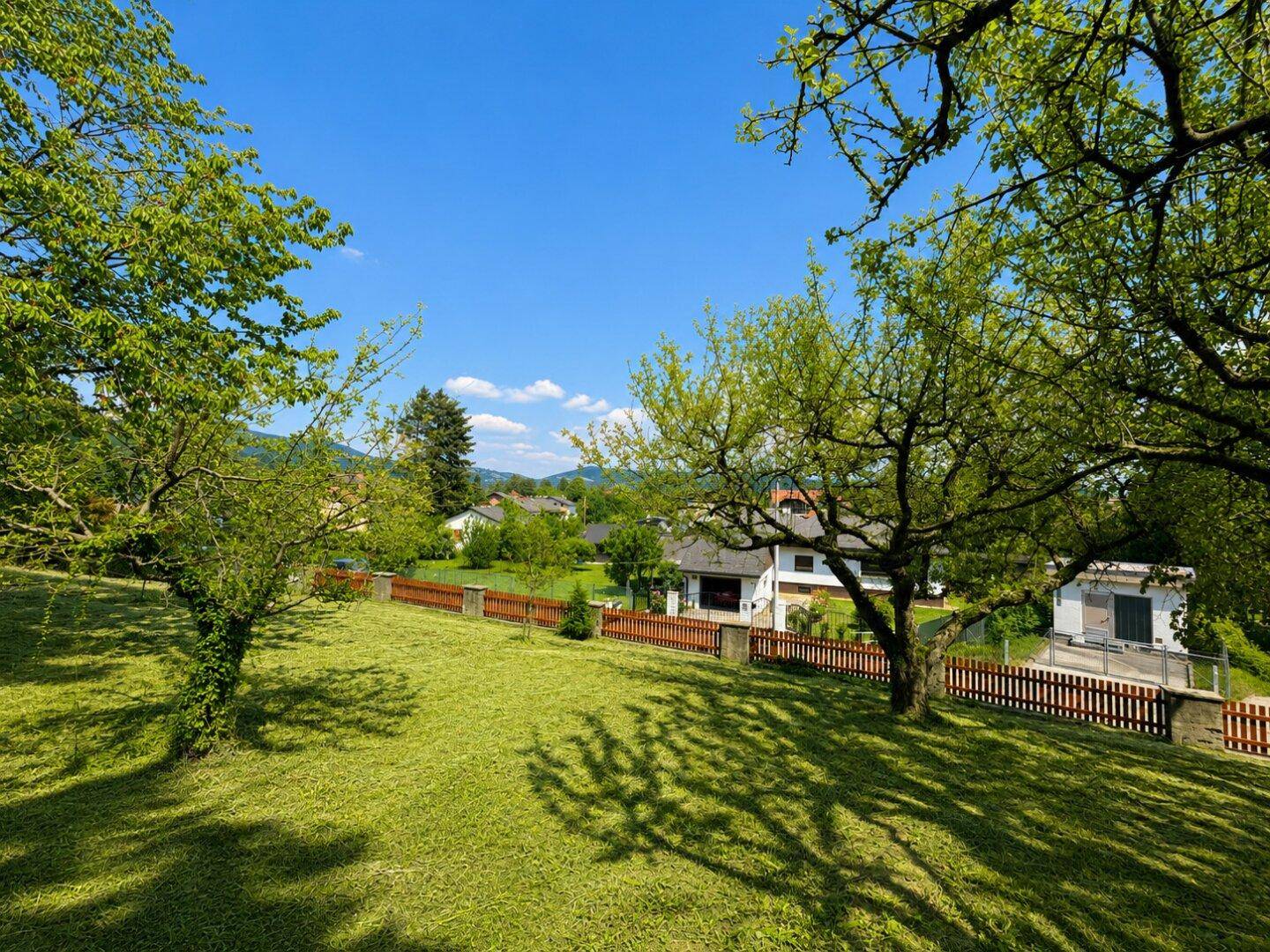 Weitläufiger Garten mit gepflegtem Rasen, Obstbäumen und Blick auf die umliegende Landschaft.