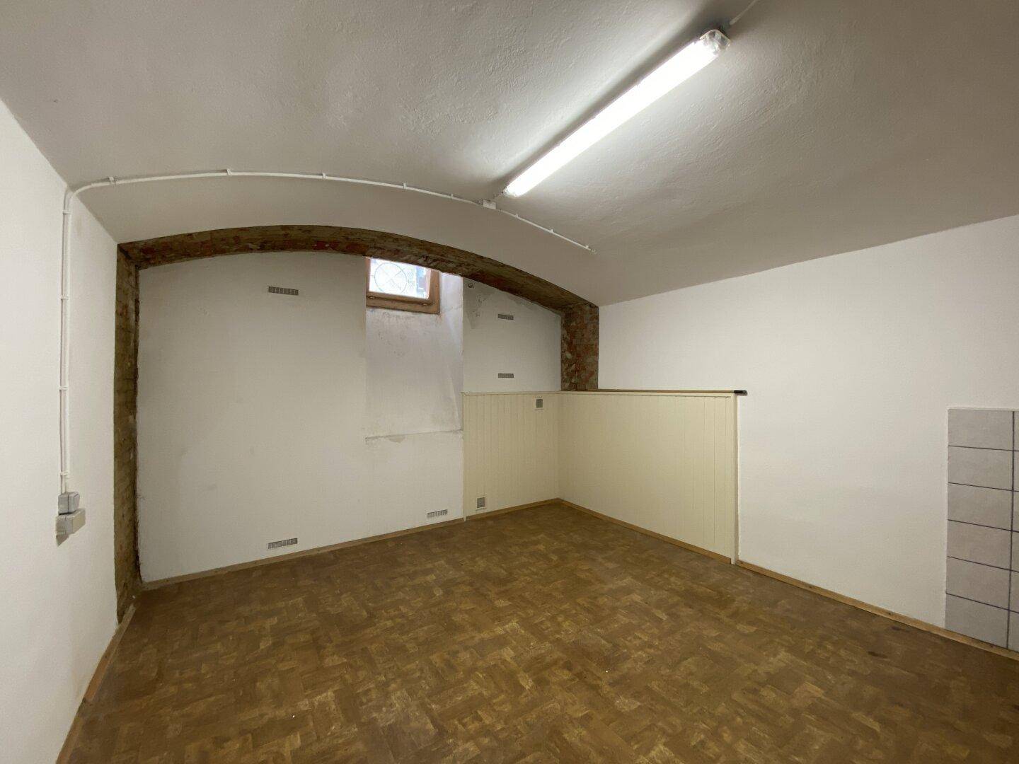 Heller Kellerraum mit Laminatboden, gewölbter Decke und unverputzten Ziegeln im Durchgangsbereich.
