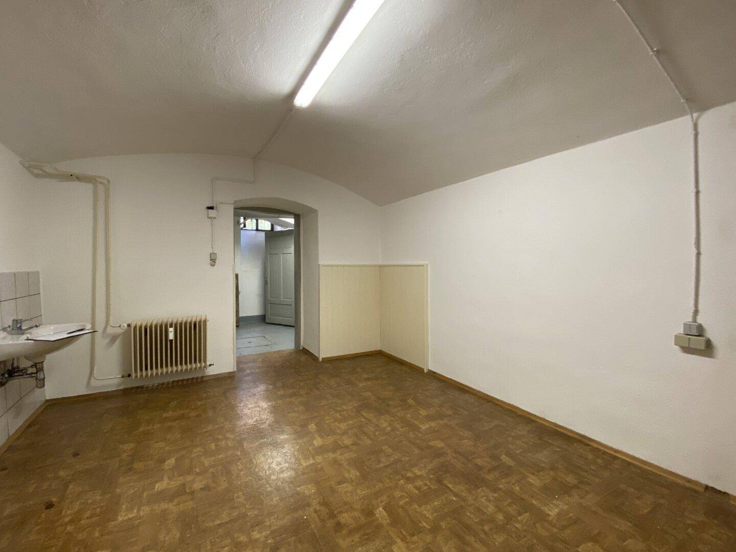 Praktischer Kellerraum mit Waschbecken, Heizung und Durchgang zu angrenzenden Räumen.