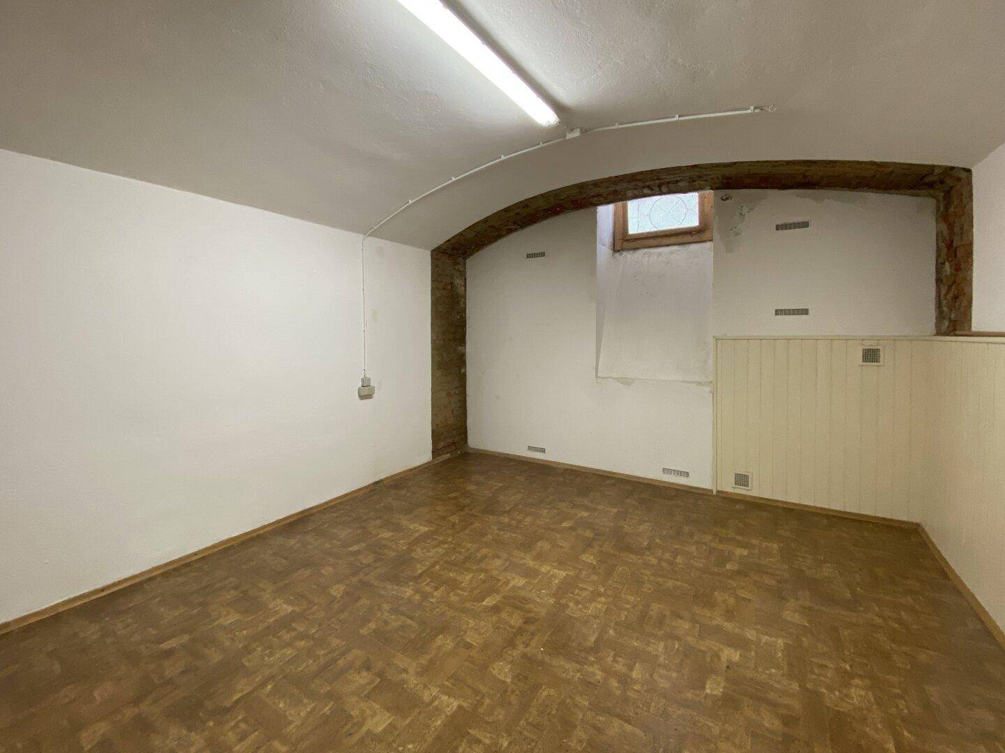 Geräumiger Kellerraum mit Holzboden, weiß gestrichenen Wänden und einem kleinen Fenster.