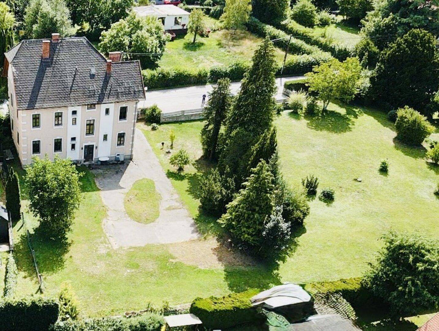 Luftaufnahme des großen Hauses mit weitläufigem Gartenbereich und Zufahrt.