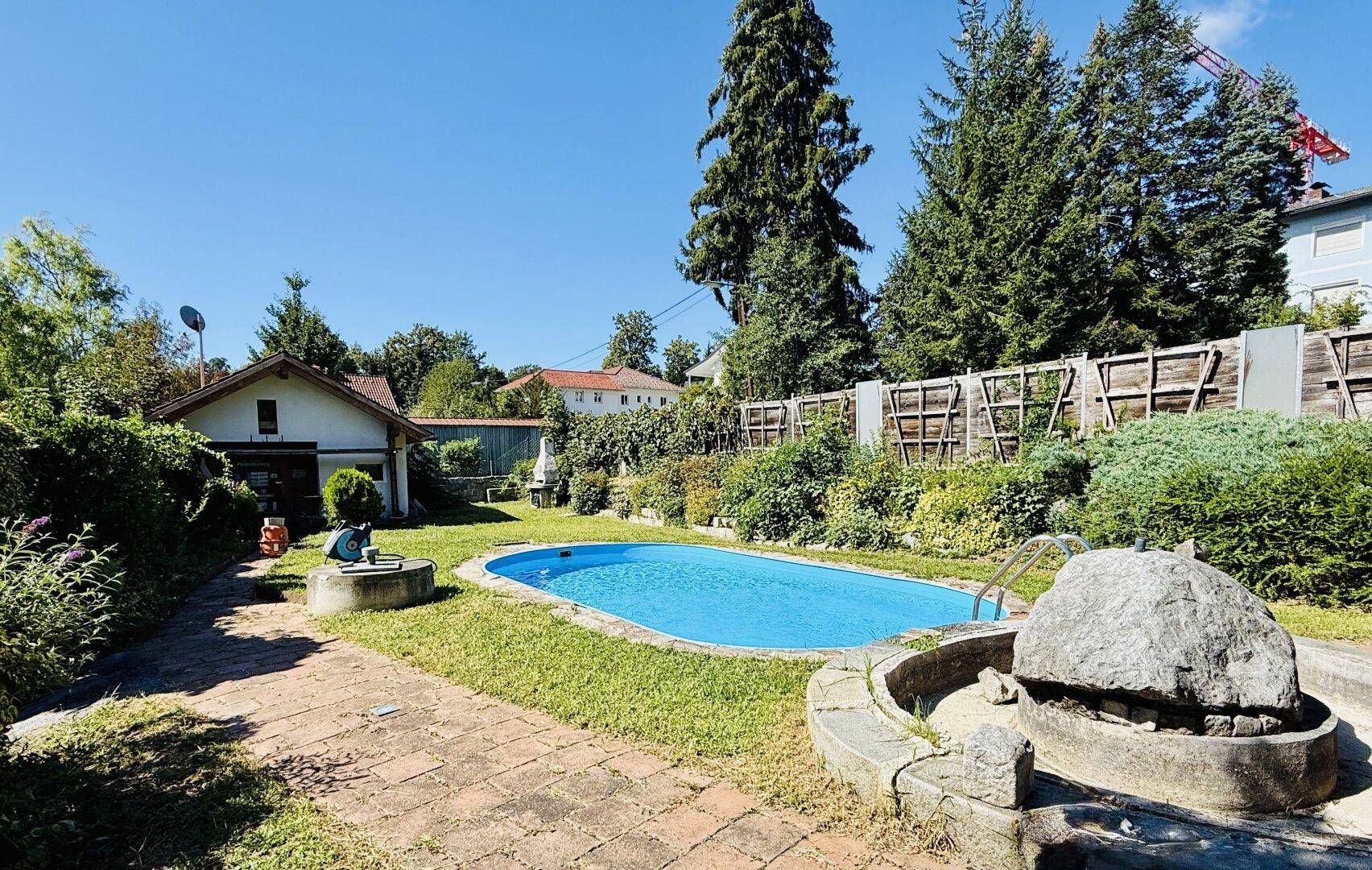 Weitläufiger Gartenbereich mit Swimmingpool, gepflastertem Weg und Nebengebäude.
