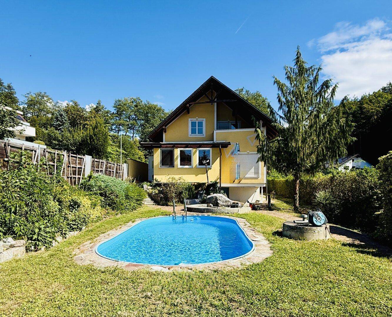 Idyllischer Garten mit Swimmingpool vor dem gelben Wohnhaus an einem sonnigen Tag.