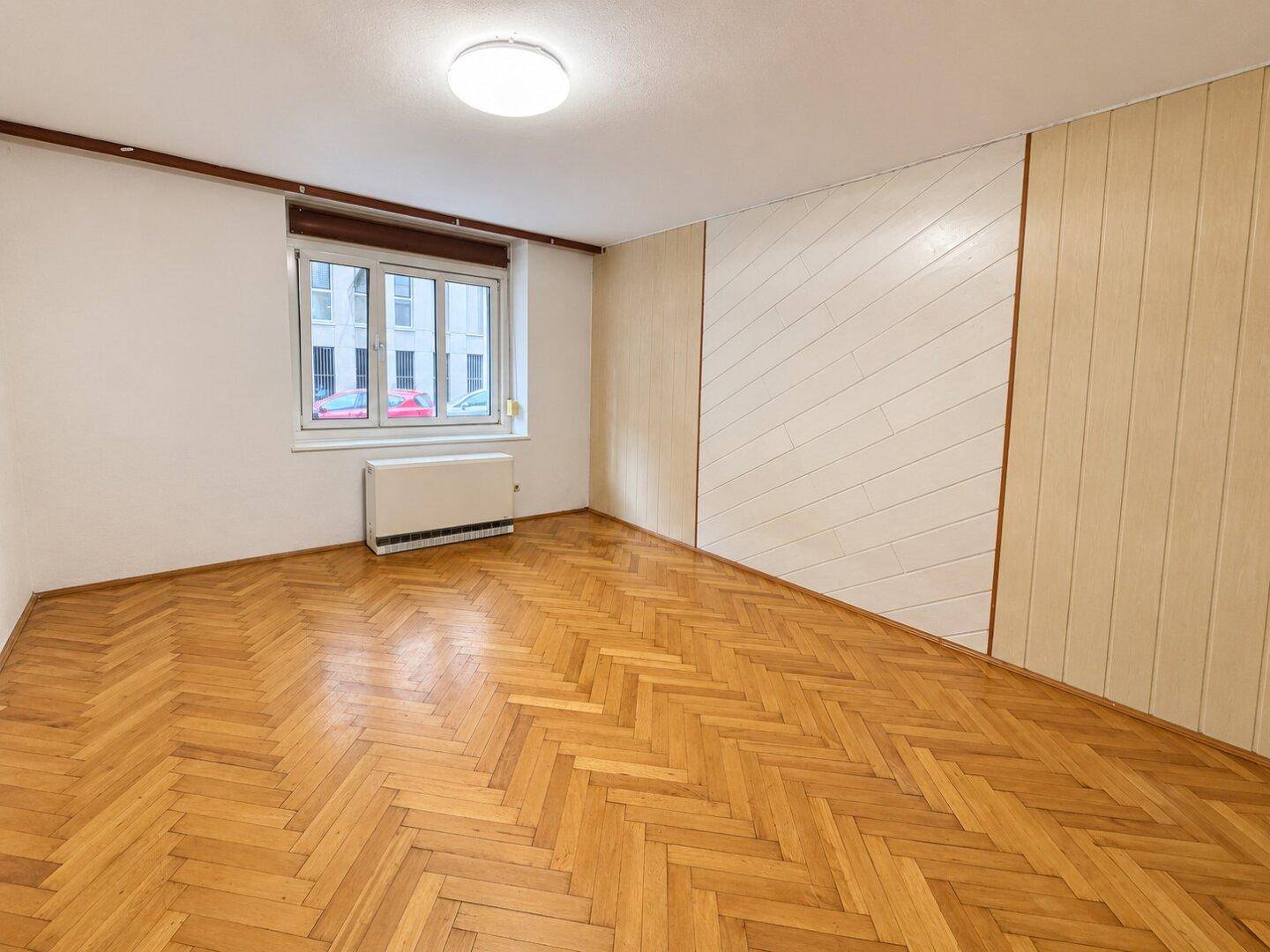 Geräumiges Zimmer mit Fischgrätparkett und heller Wandverkleidung, ideal als Wohn- oder Schlafzimmer.