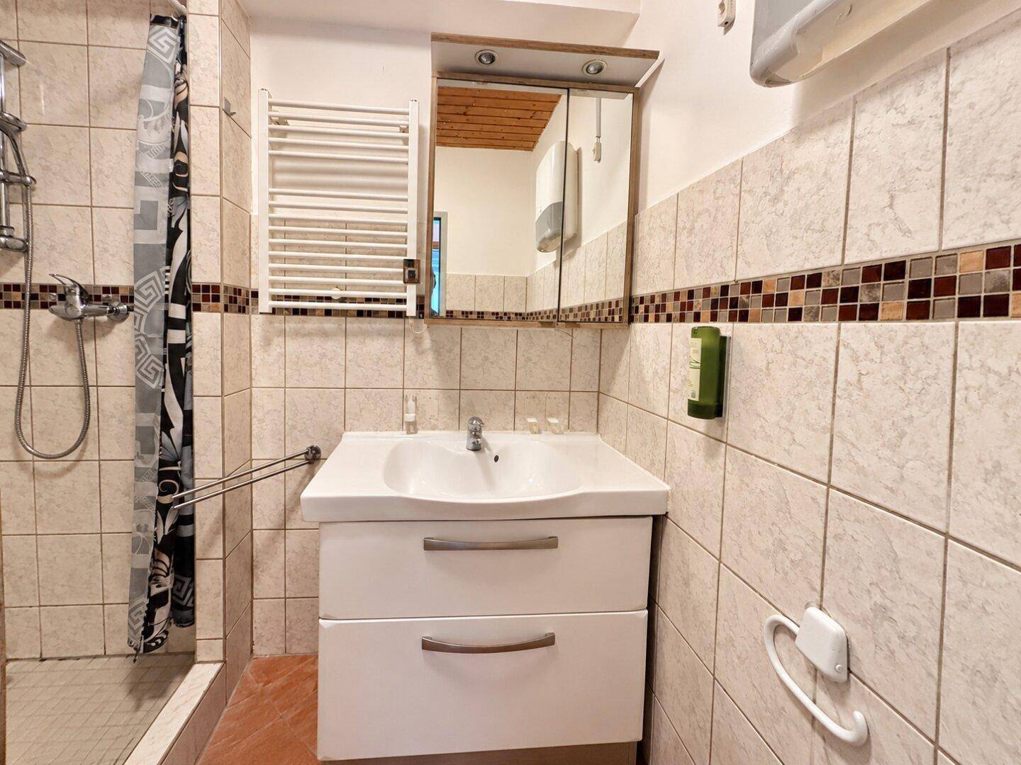 Badezimmer mit Duschbereich, Waschbeckenunterschrank und beheiztem Handtuchhalter, in gutem Zustand.