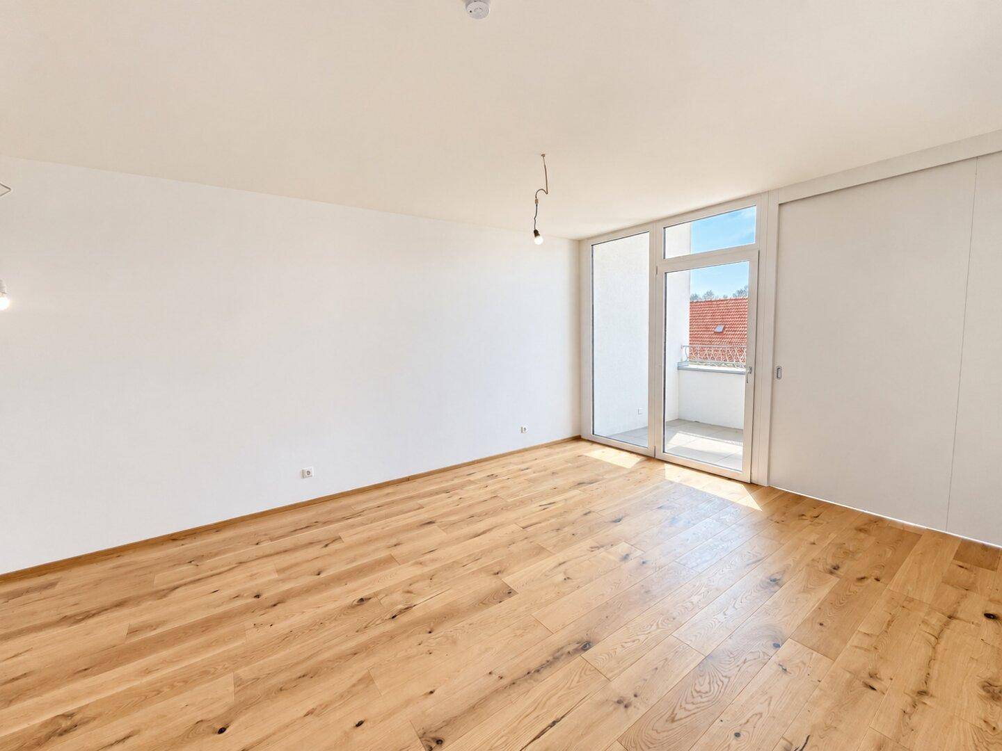 Heller, leerer Raum mit modernem Holzboden und Zugang zu einem kleinen Balkon.