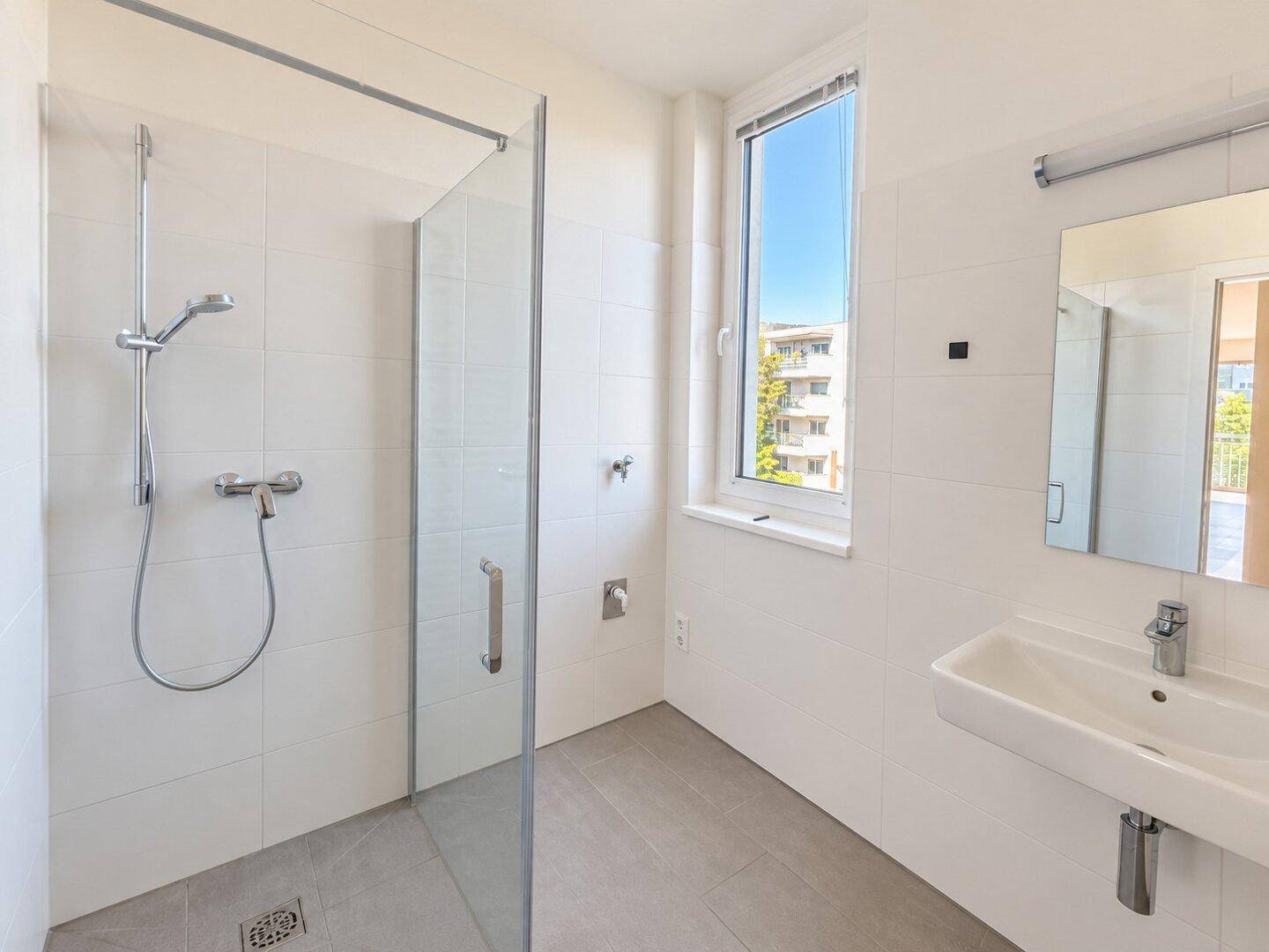 Modernes Badezimmer mit ebenerdiger Dusche, großformatigen Fliesen und einem Fenster.
