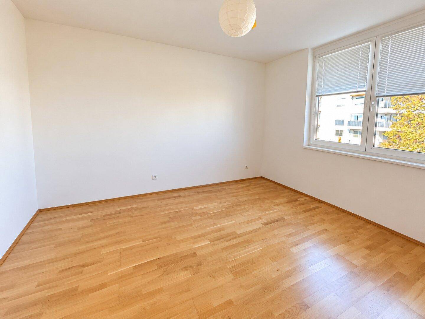 Ruhiges Schlafzimmer mit hellem Holzboden und einem Fenster, das viel Tageslicht hereinlässt.