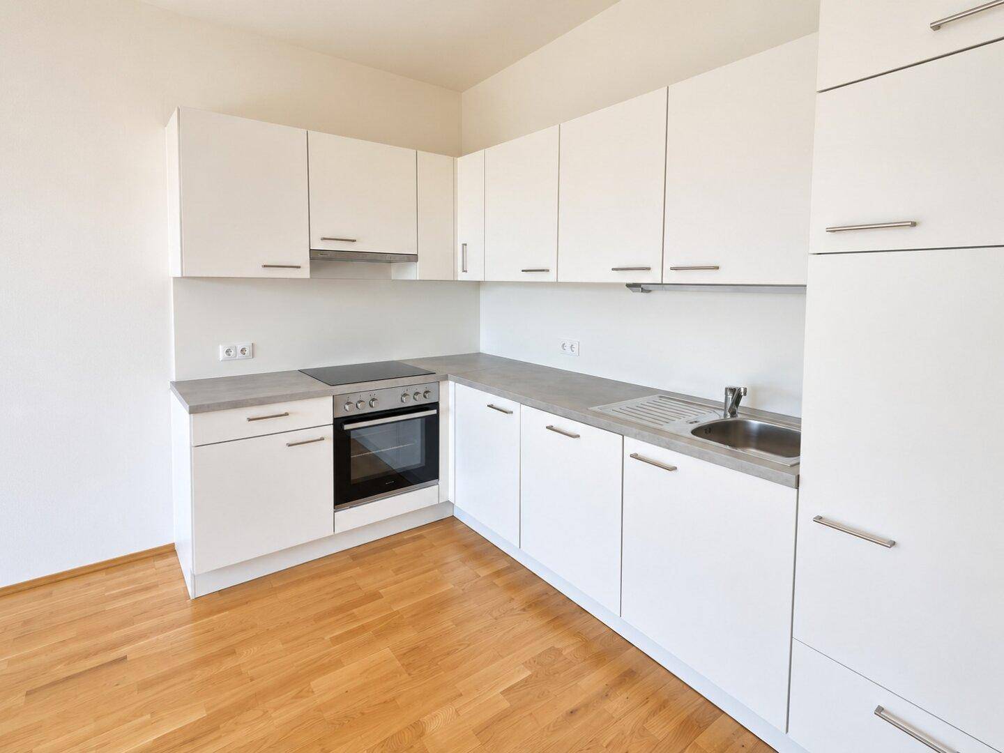 Moderne Einbauküche in Weiß mit integrierten Geräten und hellem Holzboden.