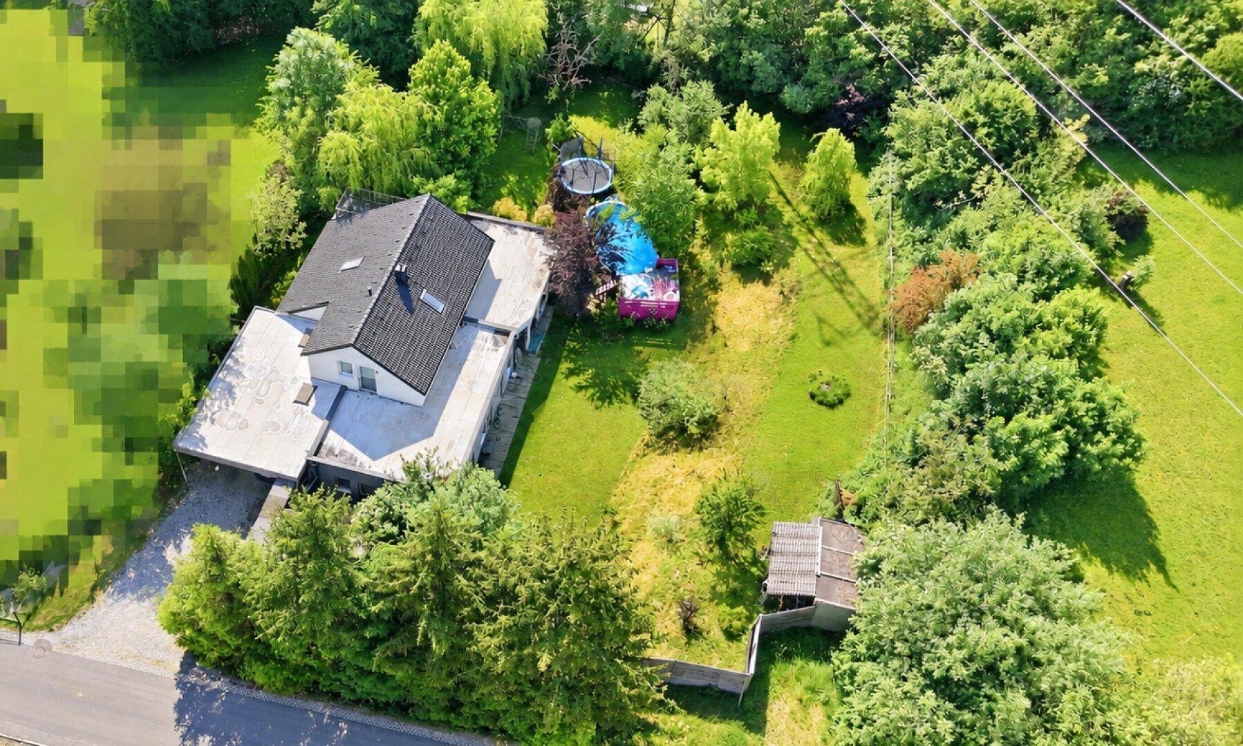 Weitläufige Luftaufnahme des Grundstücks mit Haus, Garten, Trampolin und angrenzender Natur.