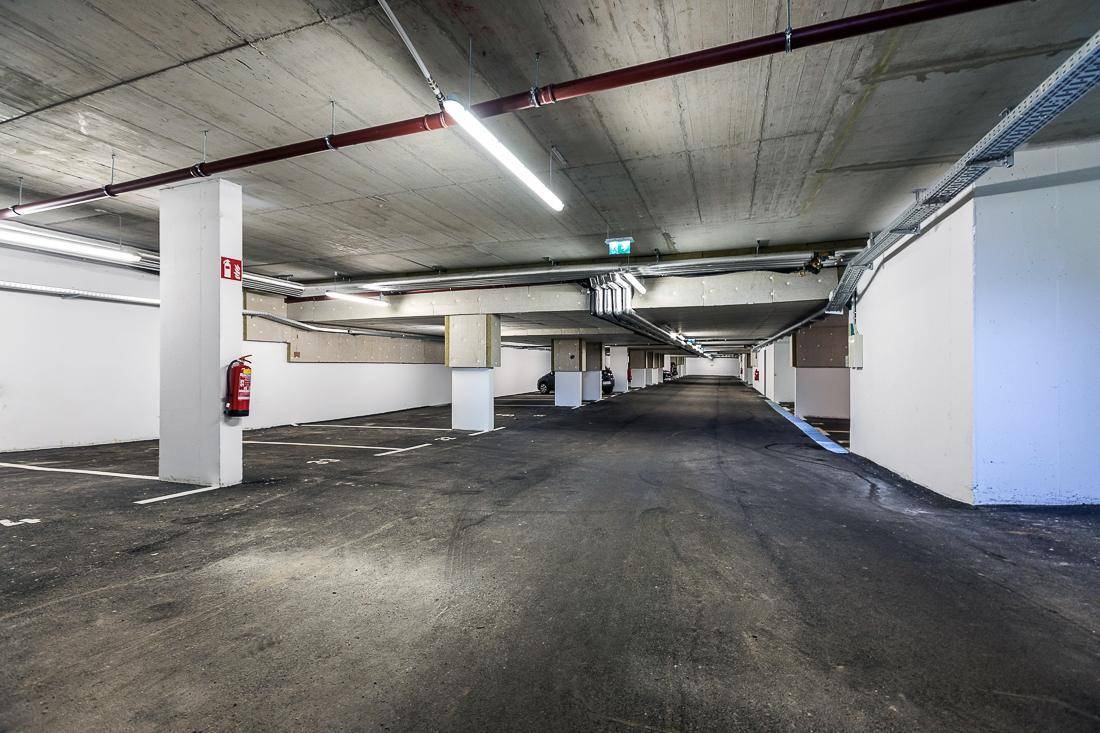 Geräumige Tiefgarage mit sichtbaren Betonstrukturen, hellen Leuchtstoffröhren und Feuerlöscher.