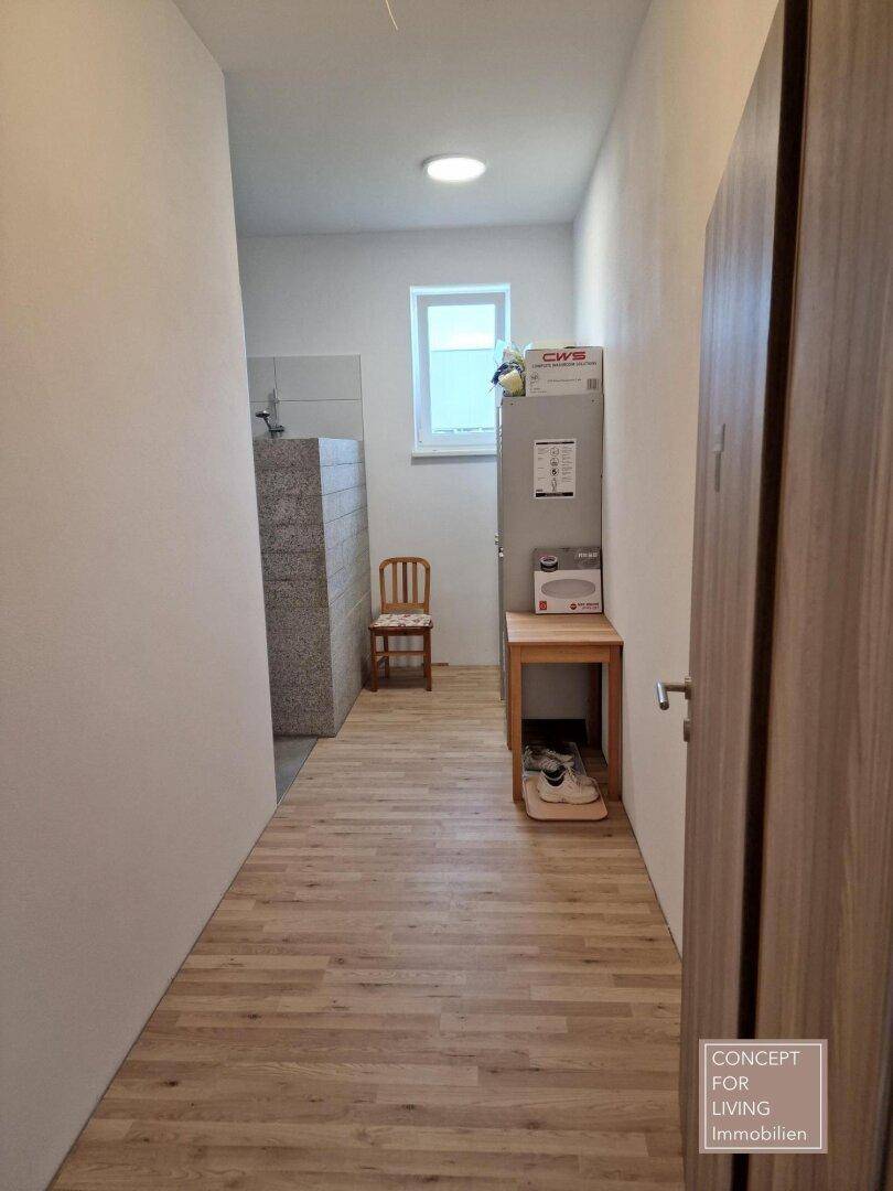 Heller Flur oder Umkleidebereich mit Holzoptik-Boden, einem kleinen Fenster und einem Waschbecken.