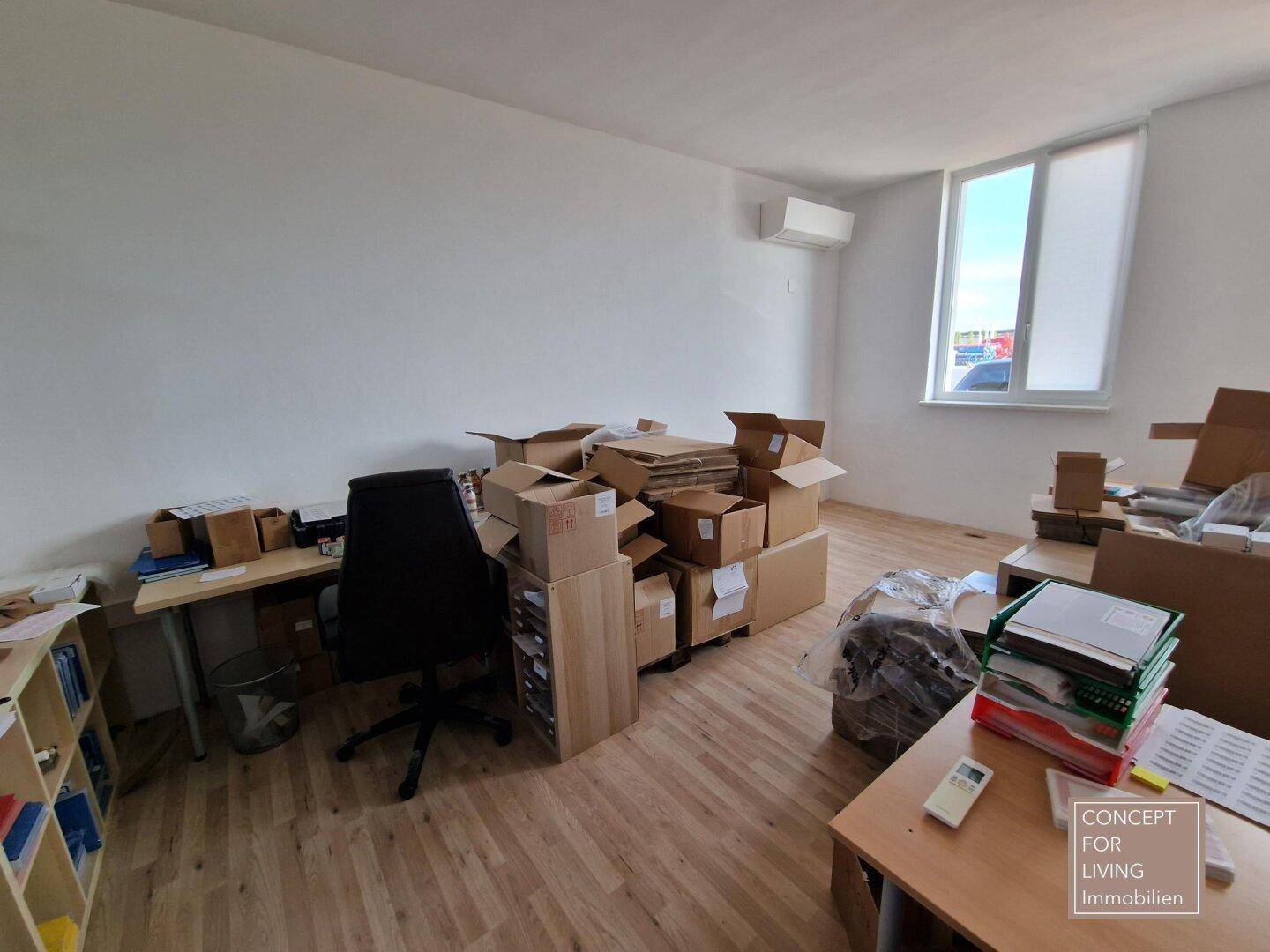 Unaufgeräumtes Büro mit vielen Kartons, Schreibtischen und einem Fenster, das Tageslicht hereinlässt.