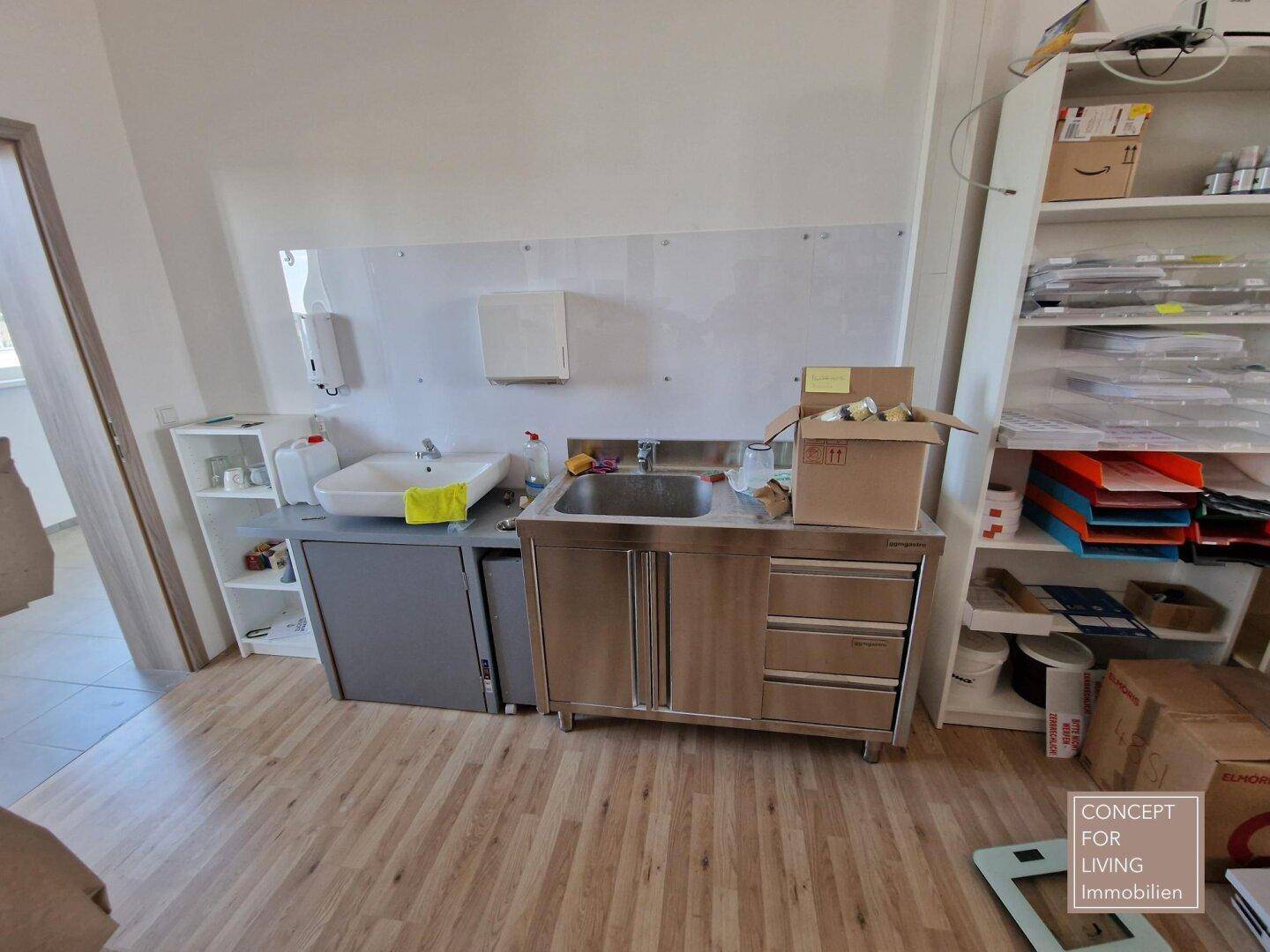 Kleiner Küchenbereich oder Waschplatz im Büro mit Spülbecken und Regalen.