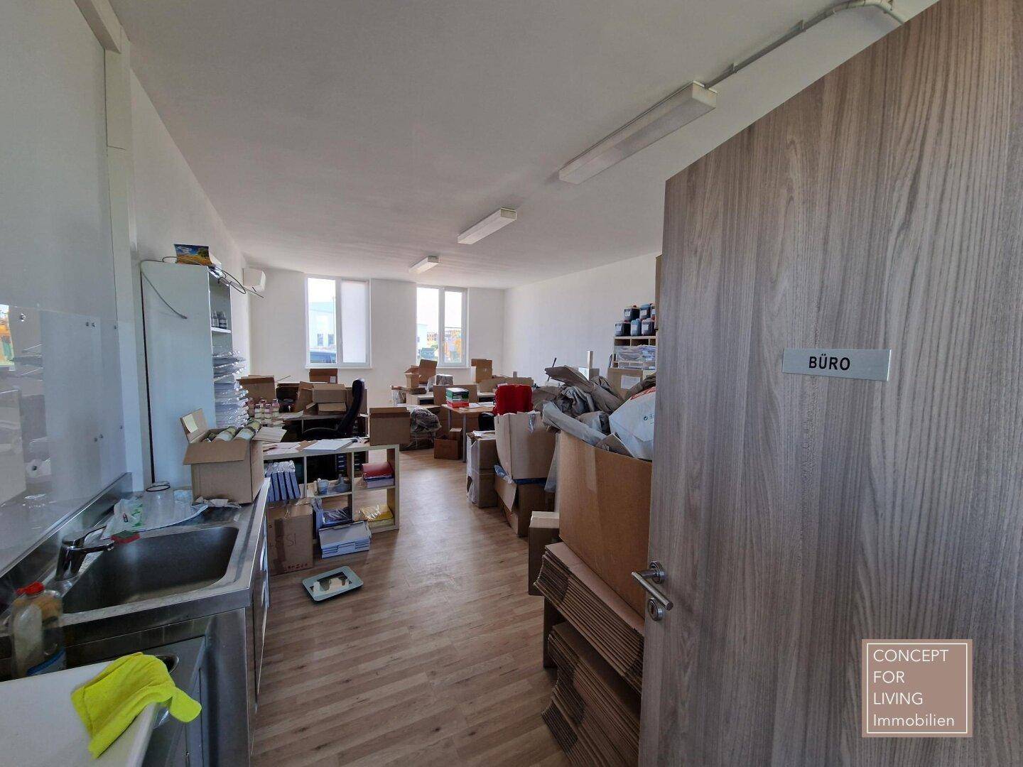 Blick in ein großes Büro mit vielen Kartons, Schreibtischen und einem Waschbeckenbereich.