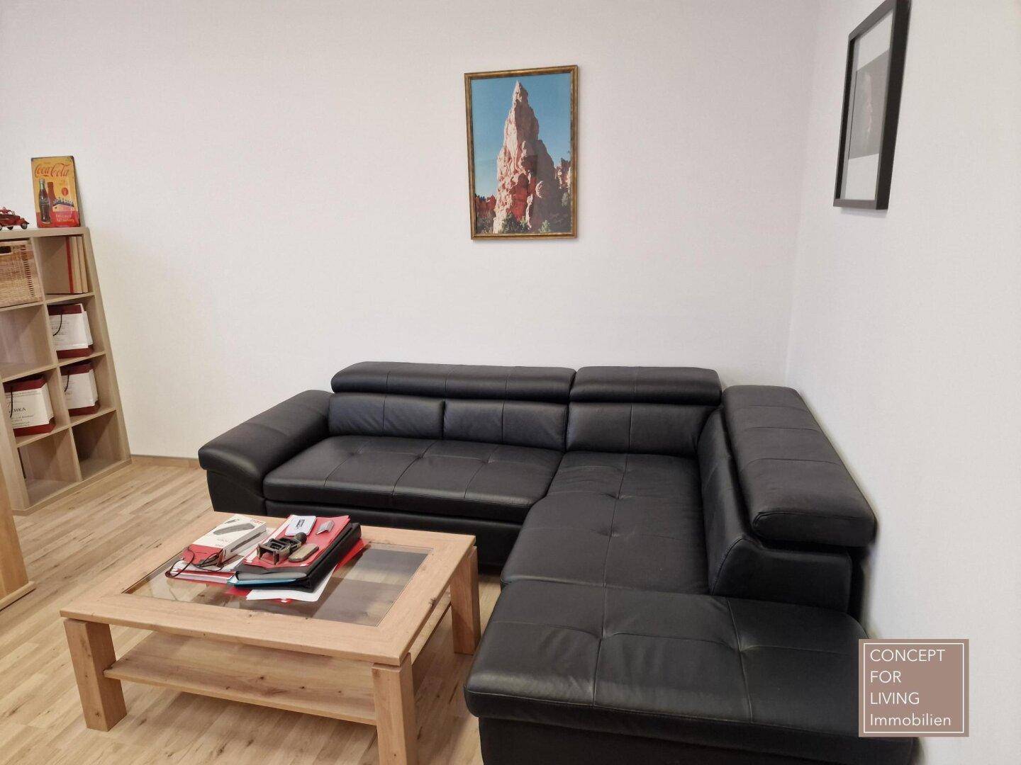 Gemütlicher Lounge-Bereich im Büro mit schwarzem Ledersofa, Couchtisch und Holzboden.
